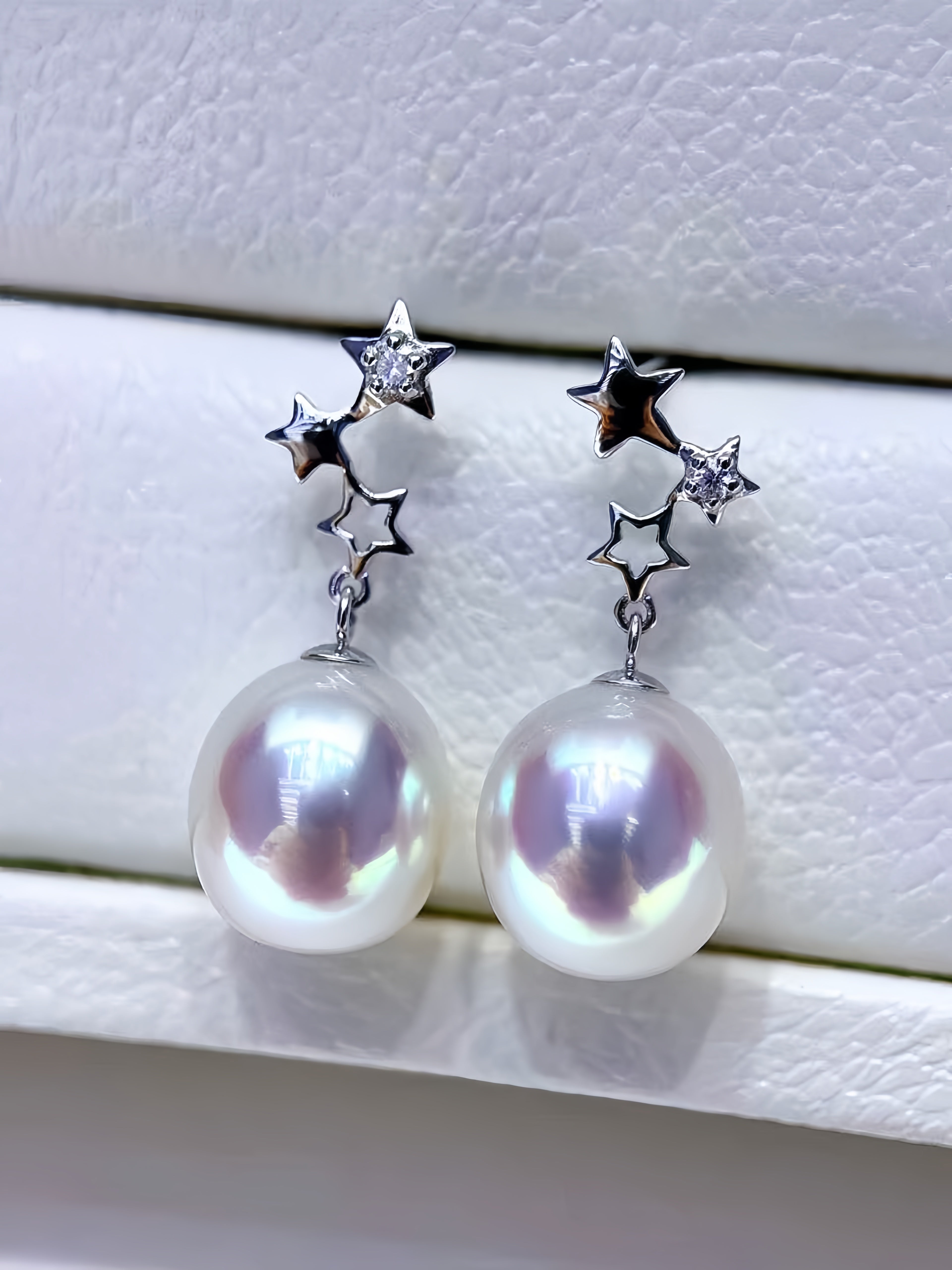 A pair of silver star drop earrings with large, lustrous white baroque pearls, displayed on a textured white surface.