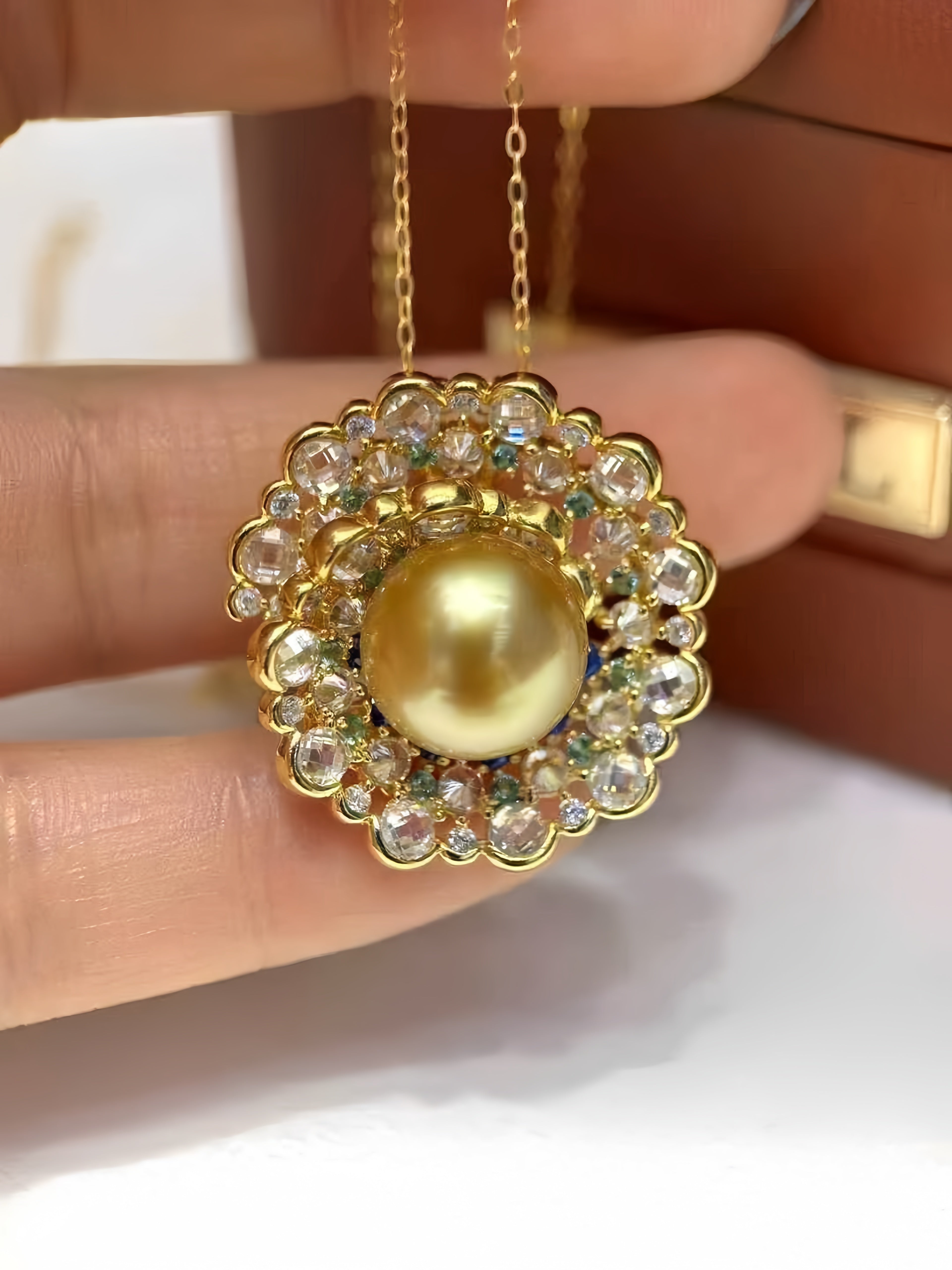 A gold pendant necklace with a large round yellow pearl surrounded by clear rhinestones, held in a hand against a brown leather background.
