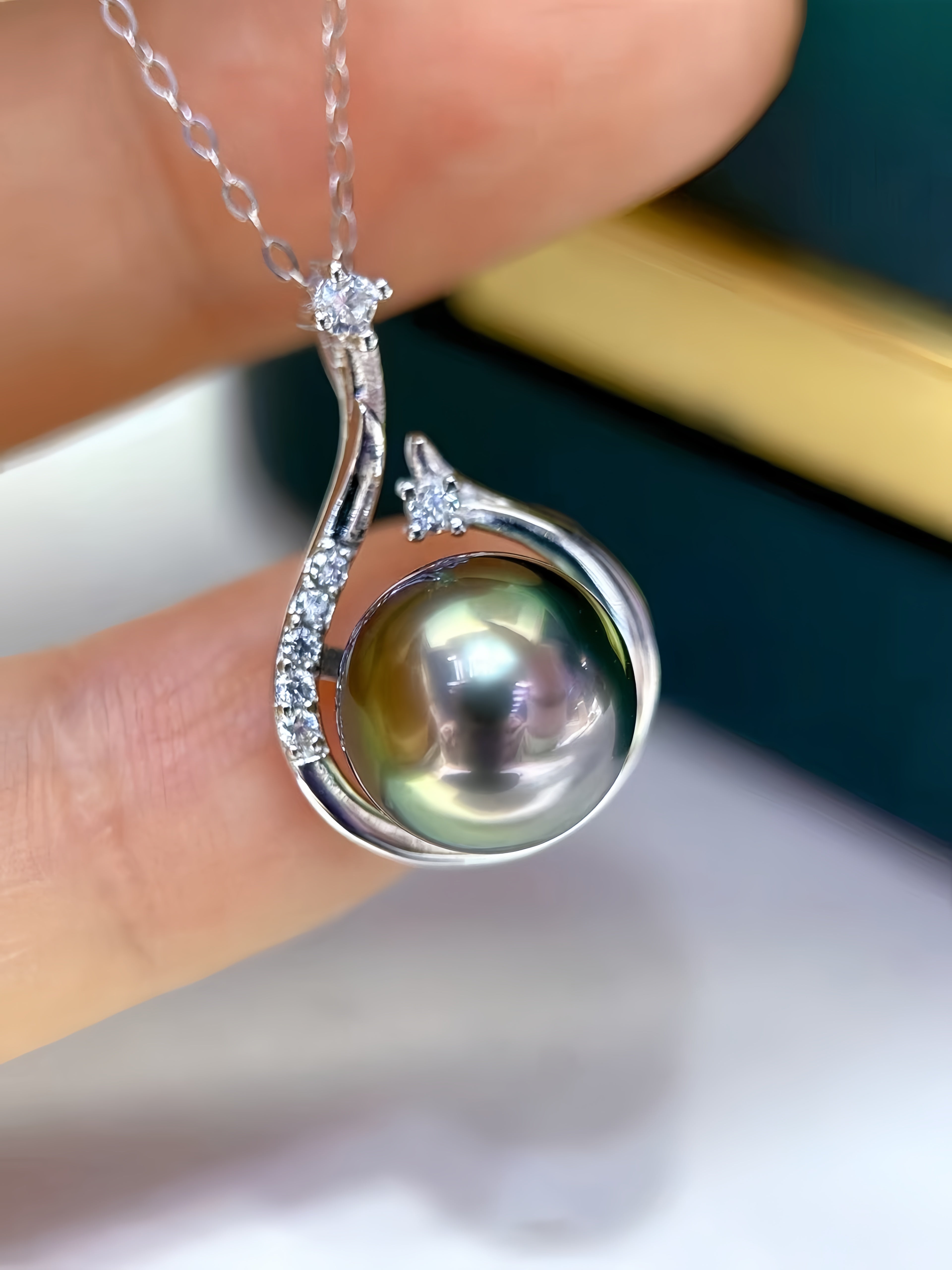 A close-up of a silver pendant necklace with a large iridescent freshwater pearl and small clear stones, held between fingers.
