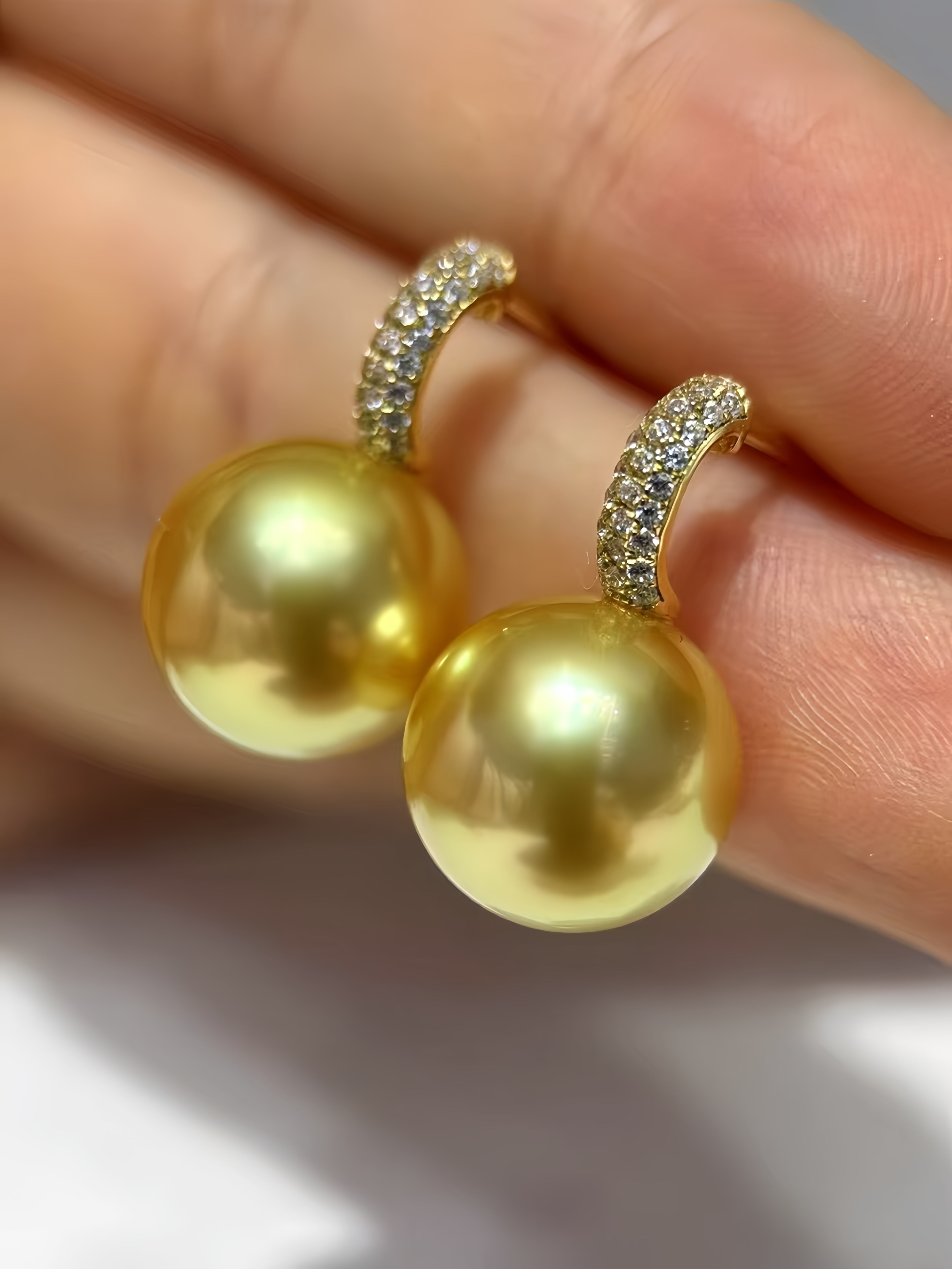 A pair of gold hoop earrings with large round yellow pearl drops and pavé-set clear stones at the hoops, shown resting on a person's fingers.