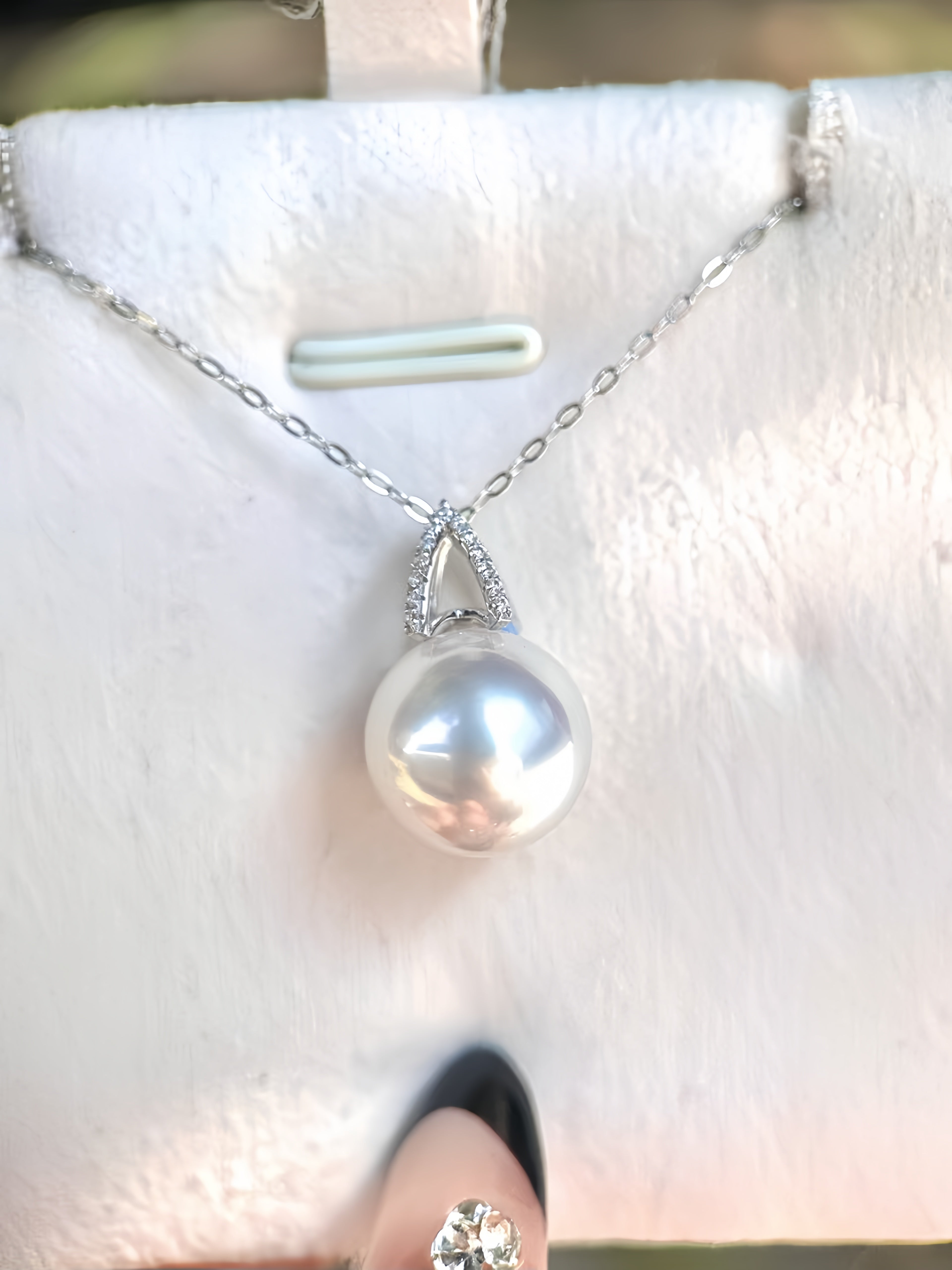 A silver pendant necklace with a single lustrous white pearl and a small diamond-accented setting, displayed on a white jewelry stand.