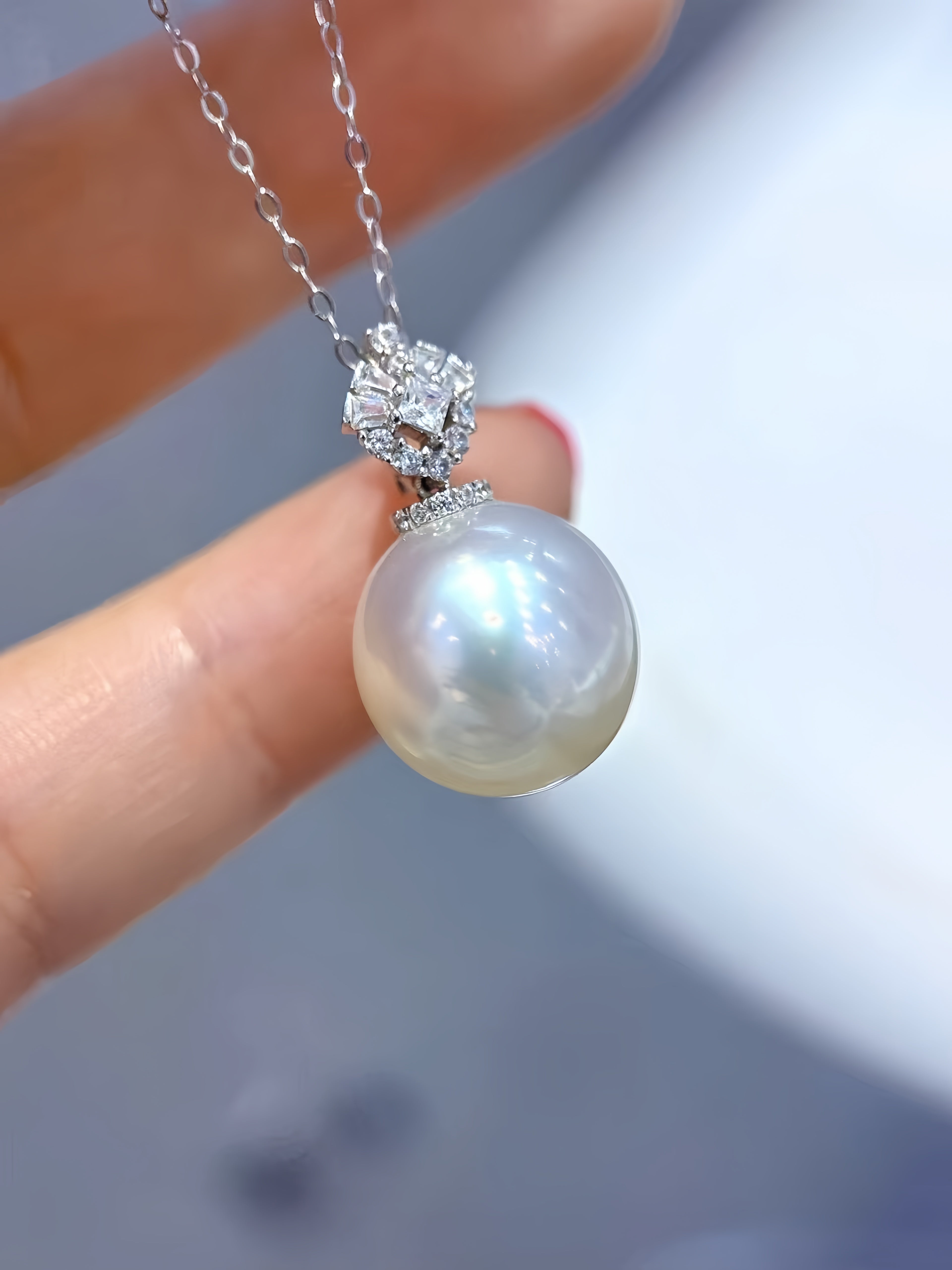 A close-up of a hand holding a silver pendant necklace featuring a large, lustrous white pearl and a sparkling silver setting.