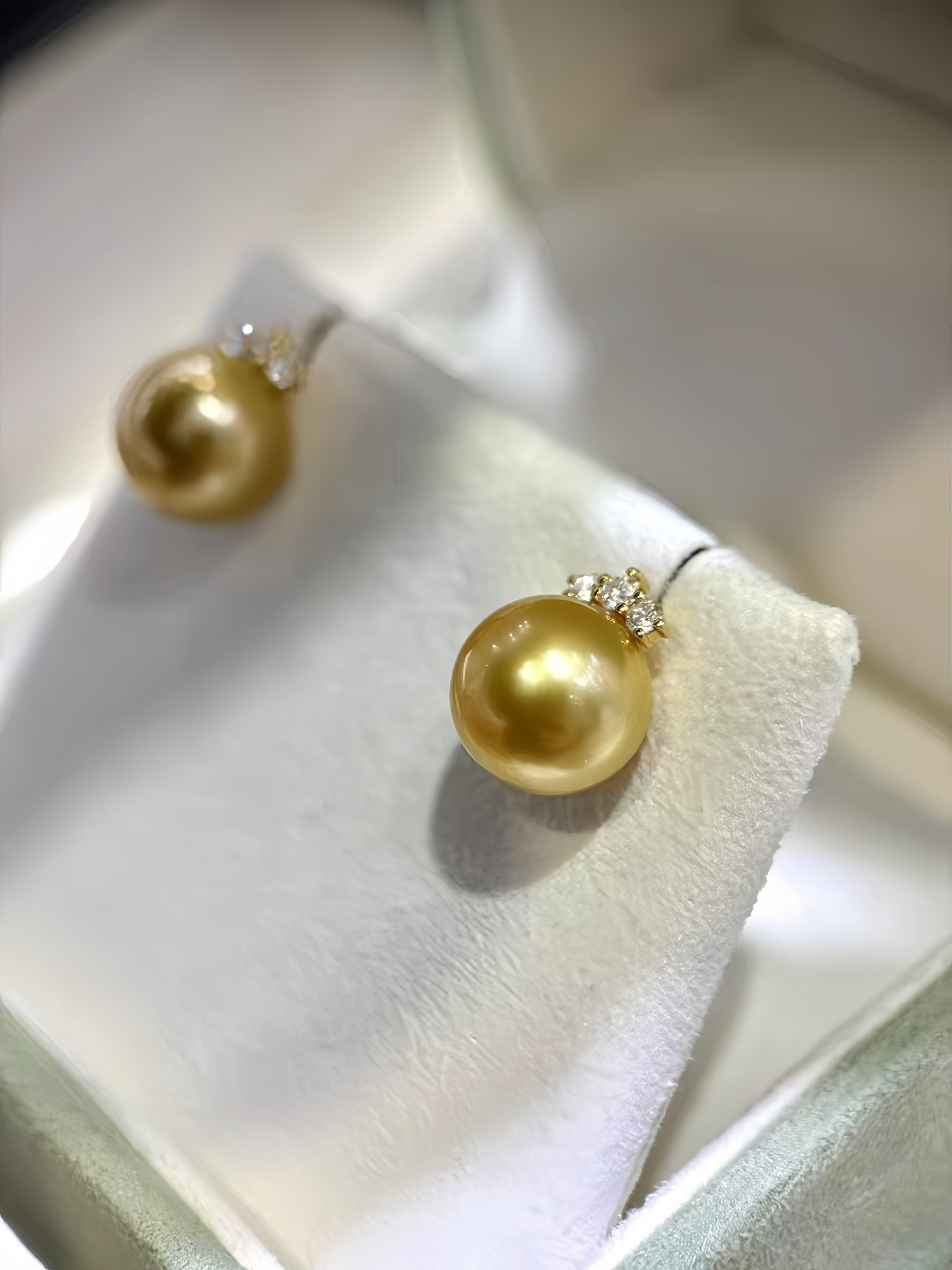 A pair of gold pearl stud earrings displayed on a white jewelry stand inside a jewelry box.