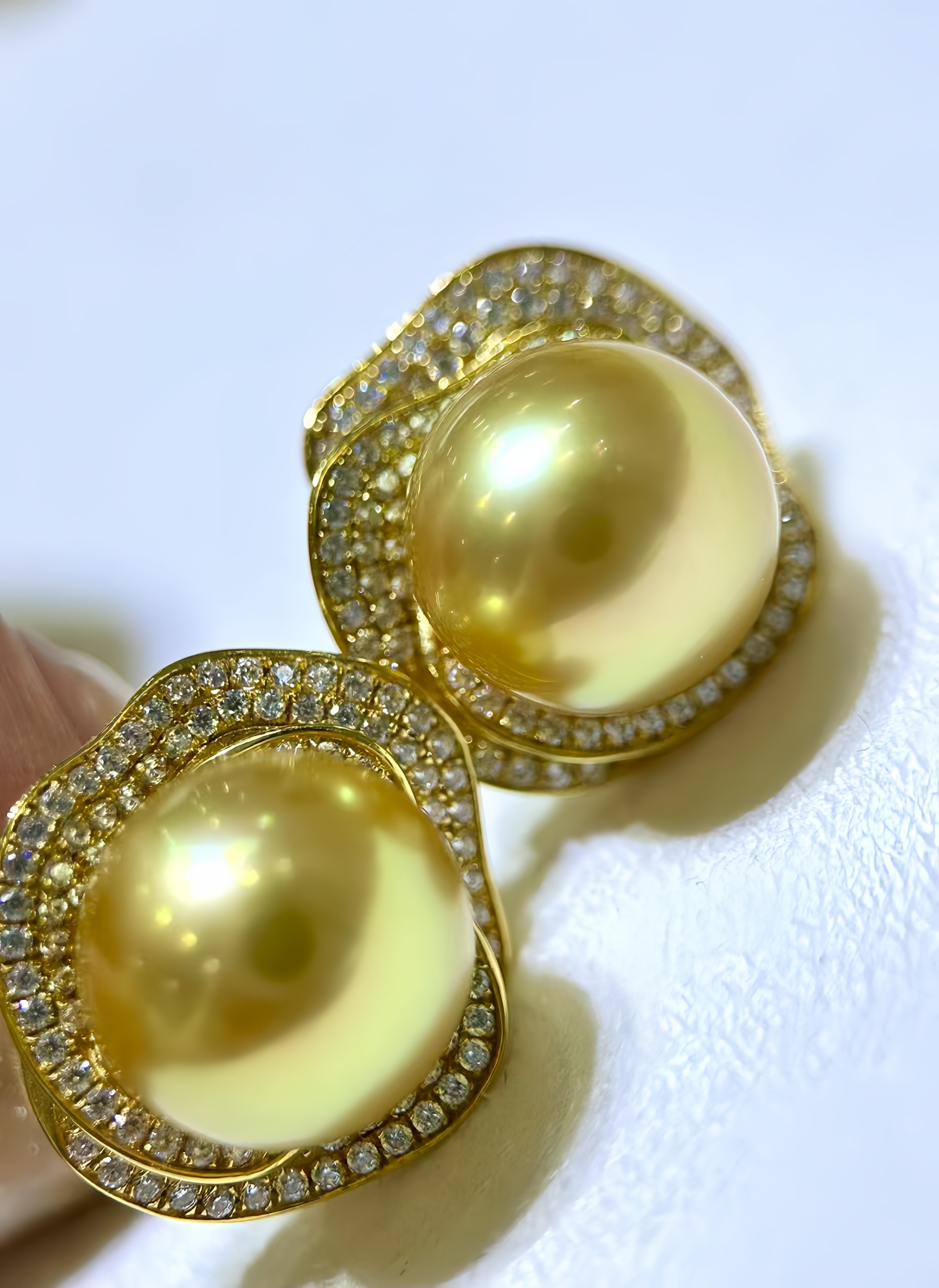A pair of gold-toned statement earrings featuring large round yellow-gold pearls surrounded by clear pavé-set stones, shown close up on a white surface.