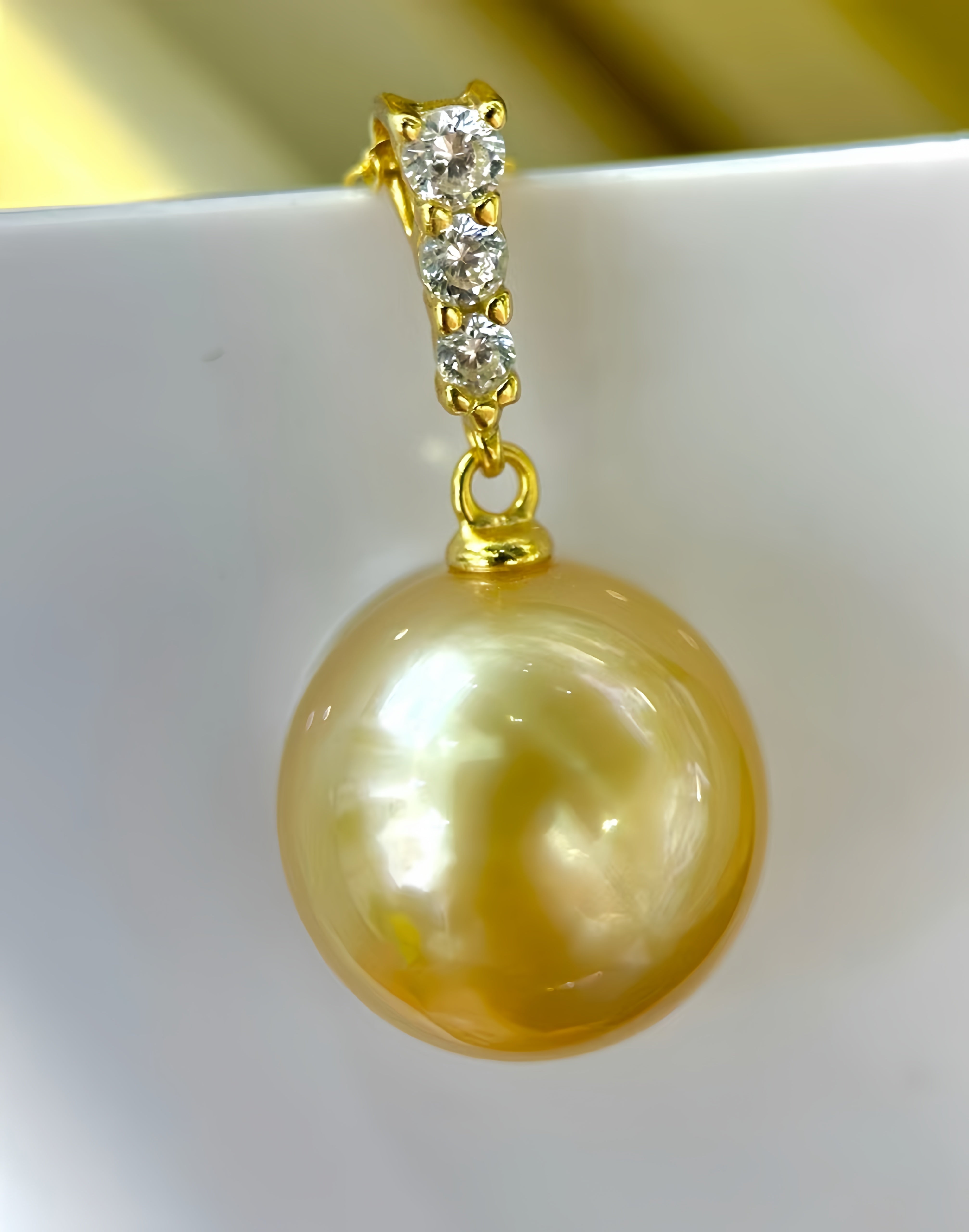 A gold pendant earring featuring a large, lustrous golden pearl and a small cluster of clear stones, displayed on a white surface.