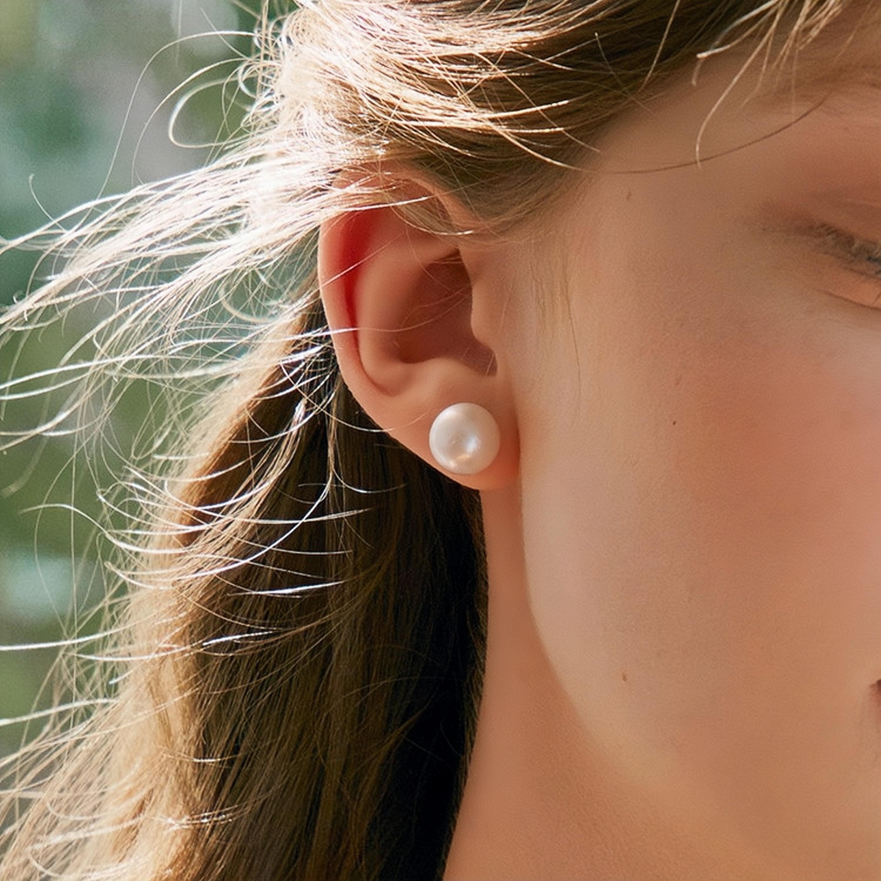 A close-up image of a woman's ear wearing a white pearl stud earring.