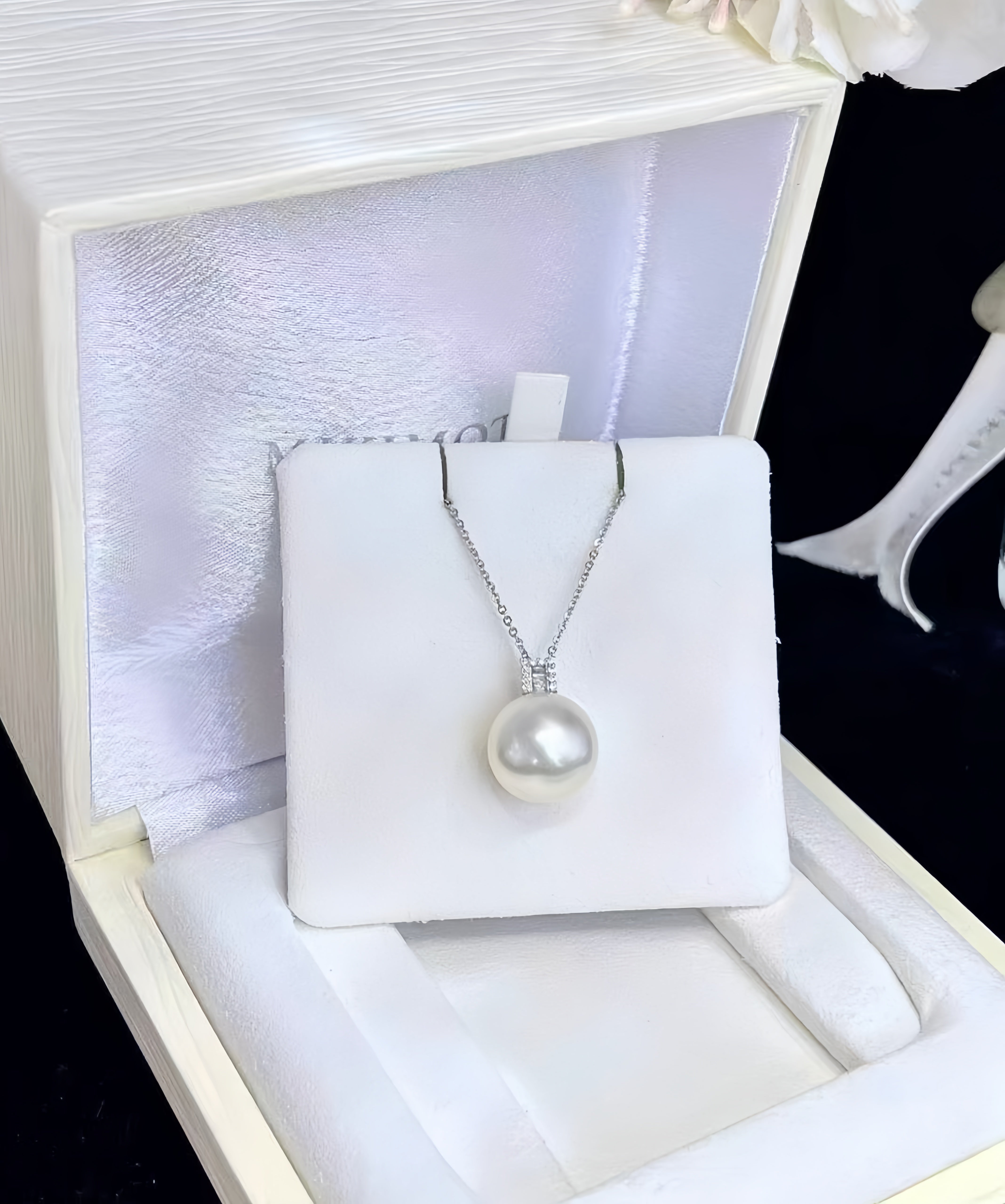 A white freshwater pearl pendant necklace on a silver chain, displayed on a white jewelry card inside an open cream-colored presentation box.