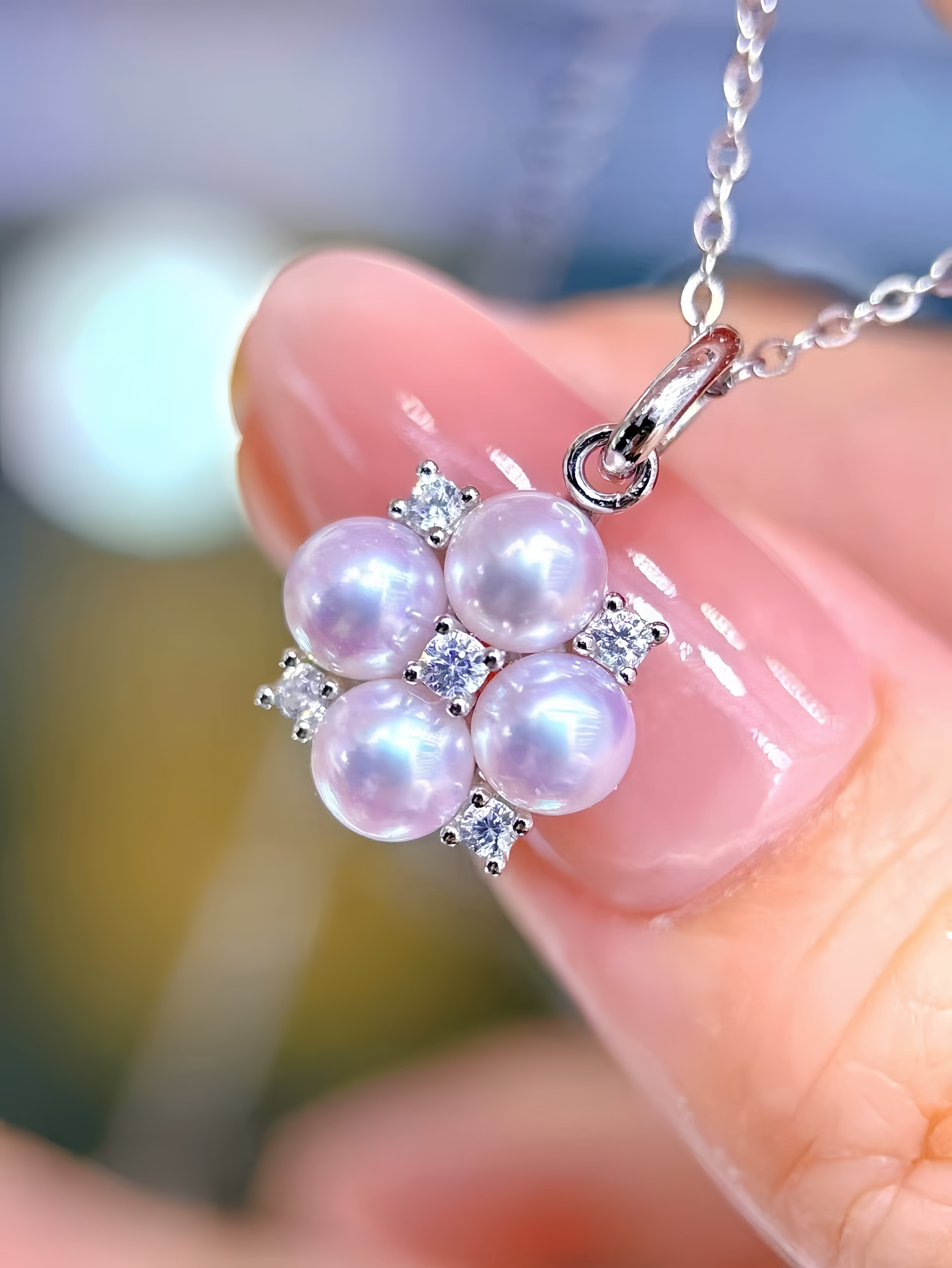 A close-up of a silver pendant necklace with five lustrous light purple pearls and small clear stones, held between fingers.