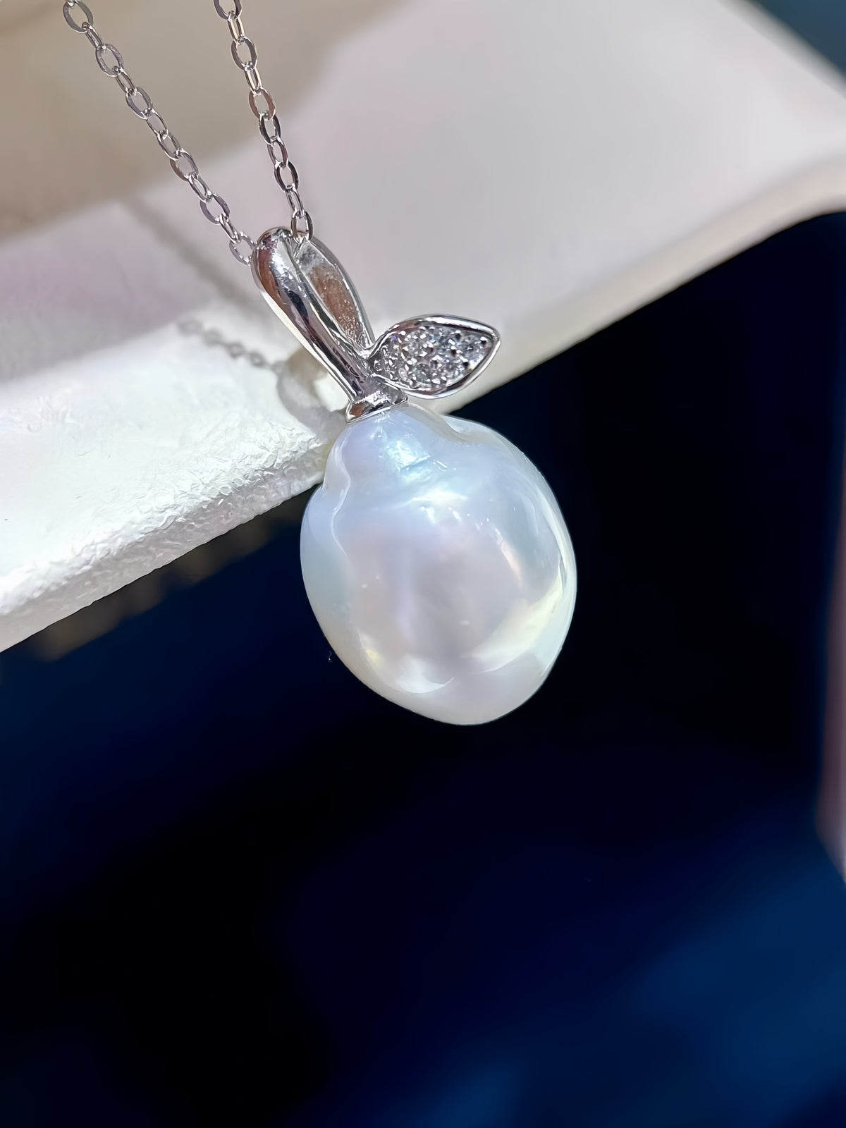 A silver pendant necklace featuring a large, lustrous white baroque pearl shaped like a bunny, with a small leaf detail on the side set with tiny clear stones, hanging from a silver chain.