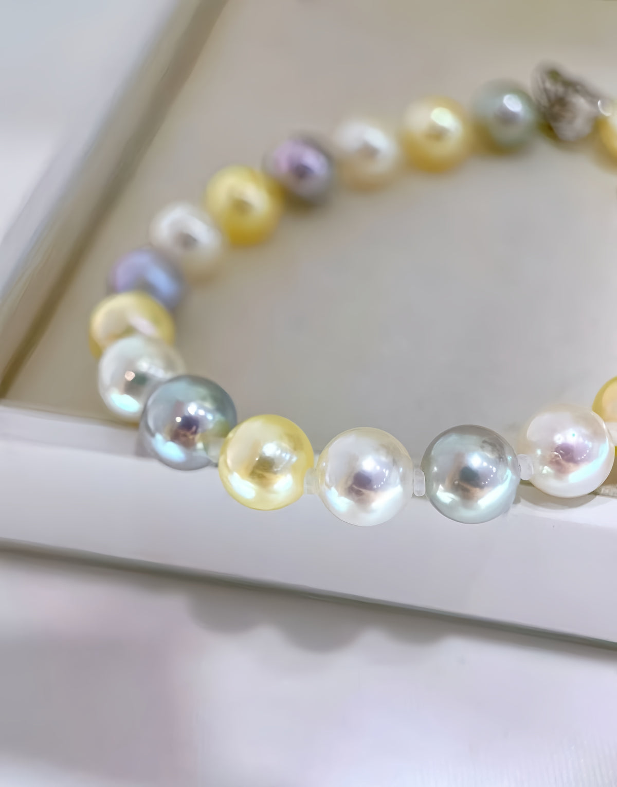 A strand of iridescent freshwater pearl beads in pastel yellow, white, lavender, and pale green, arranged in a circle on a white jewelry display box.