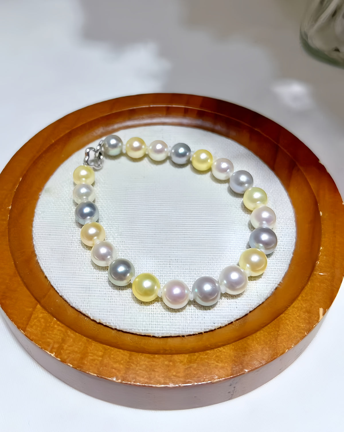A beaded pearl bracelet with mixed pastel colors including yellow, white, pink, and gray, displayed on a white fabric-lined wooden tray.