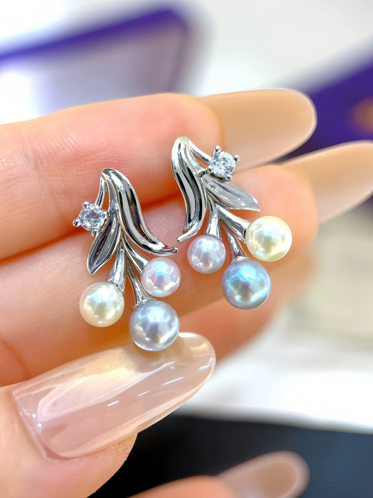 A close-up of a hand holding a pair of silver branch-shaped earrings with iridescent pearl drops and small clear stones.