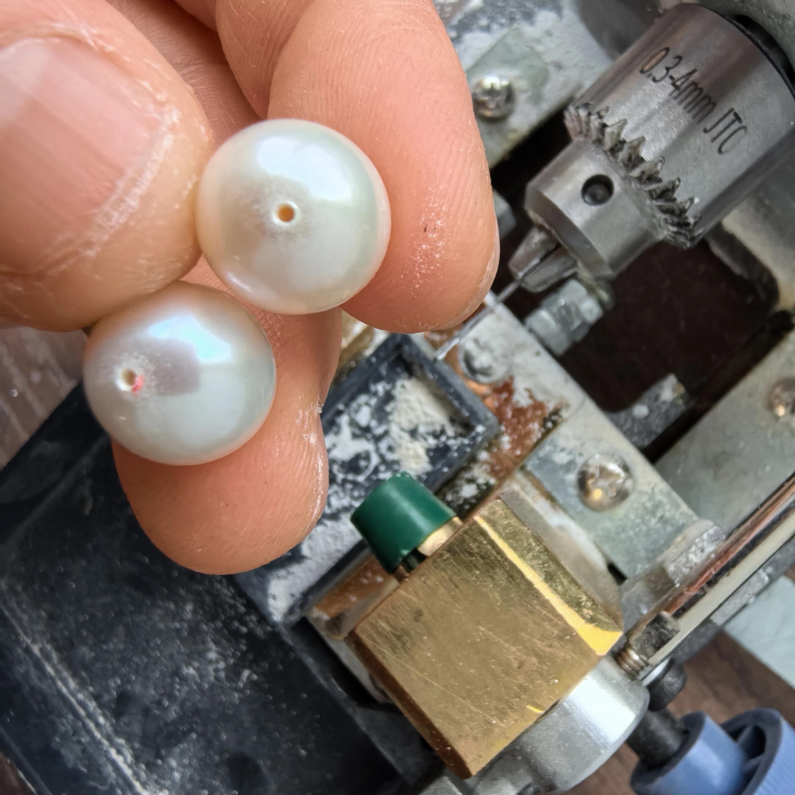 Freshwater pearl held in a padded pearl drilling vise beside micro drill bits and a caliper; setup for how to drill pearls cleanly without cracking nacre