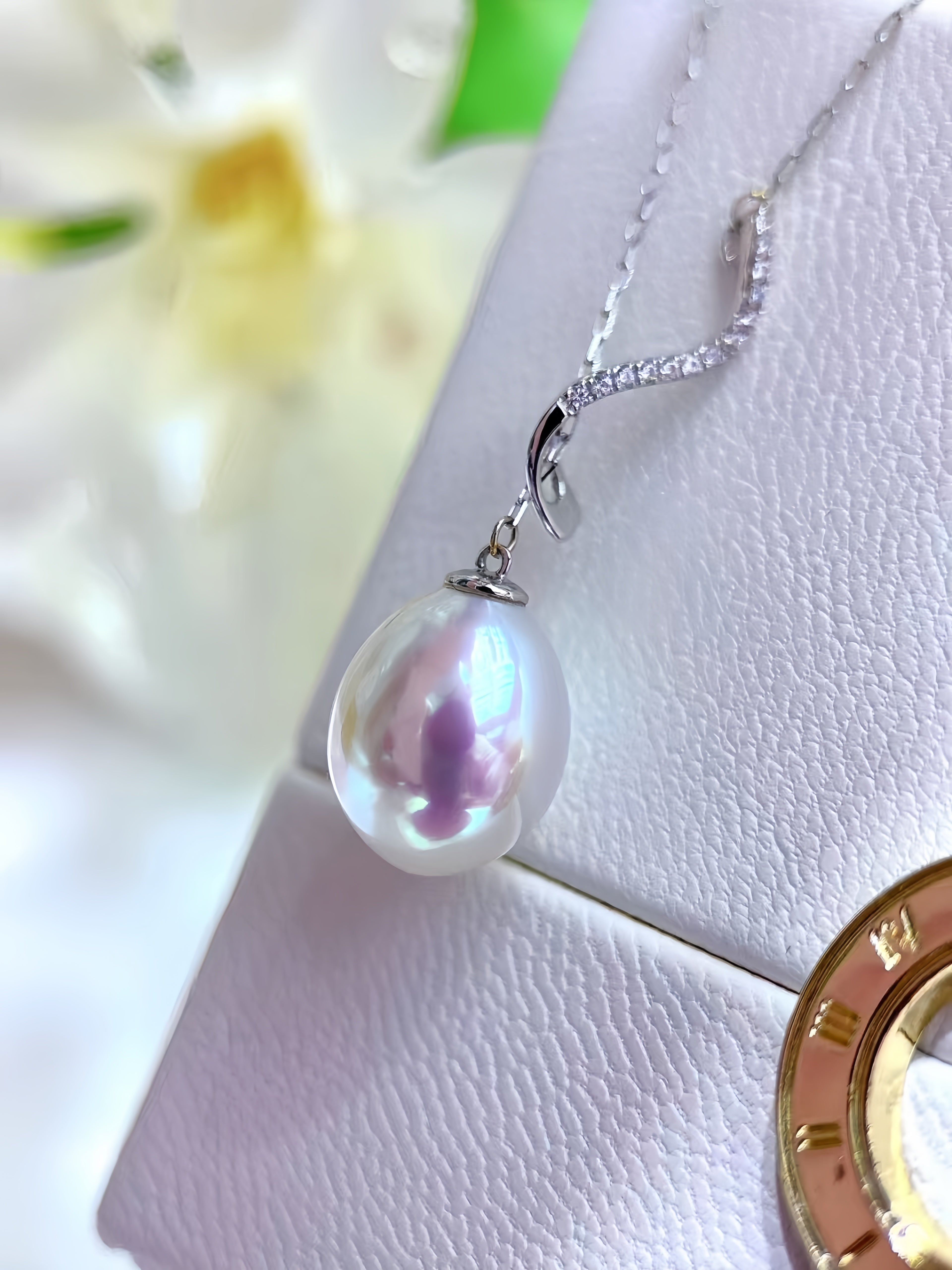 A silver necklace with a large, lustrous white freshwater pearl pendant and a pavé-set diamond chain, displayed on a textured white jewelry box.