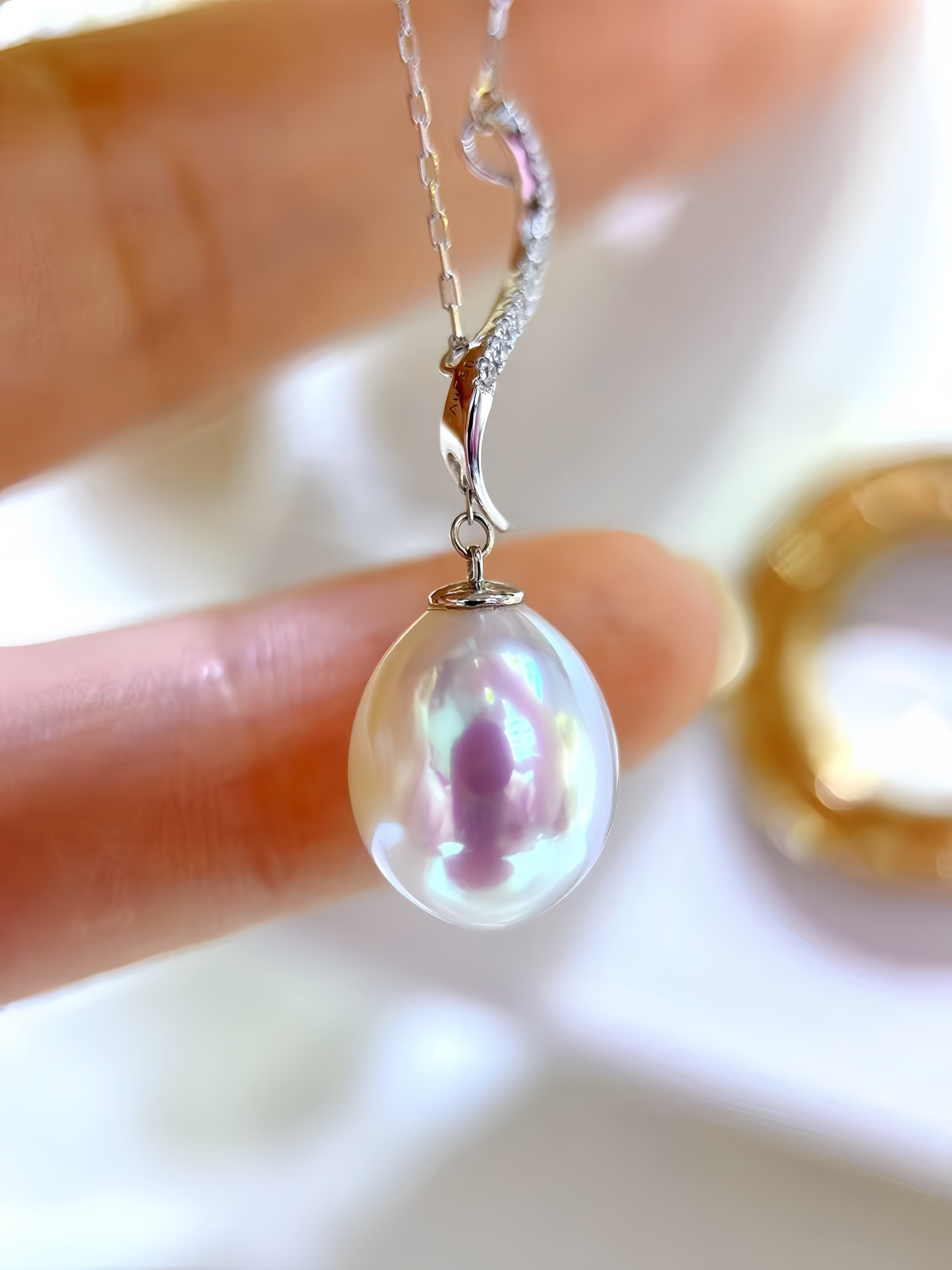 A close-up of a silver necklace with a curved, pavé-set chain and a large, lustrous iridescent freshwater pearl pendant, held between fingers.