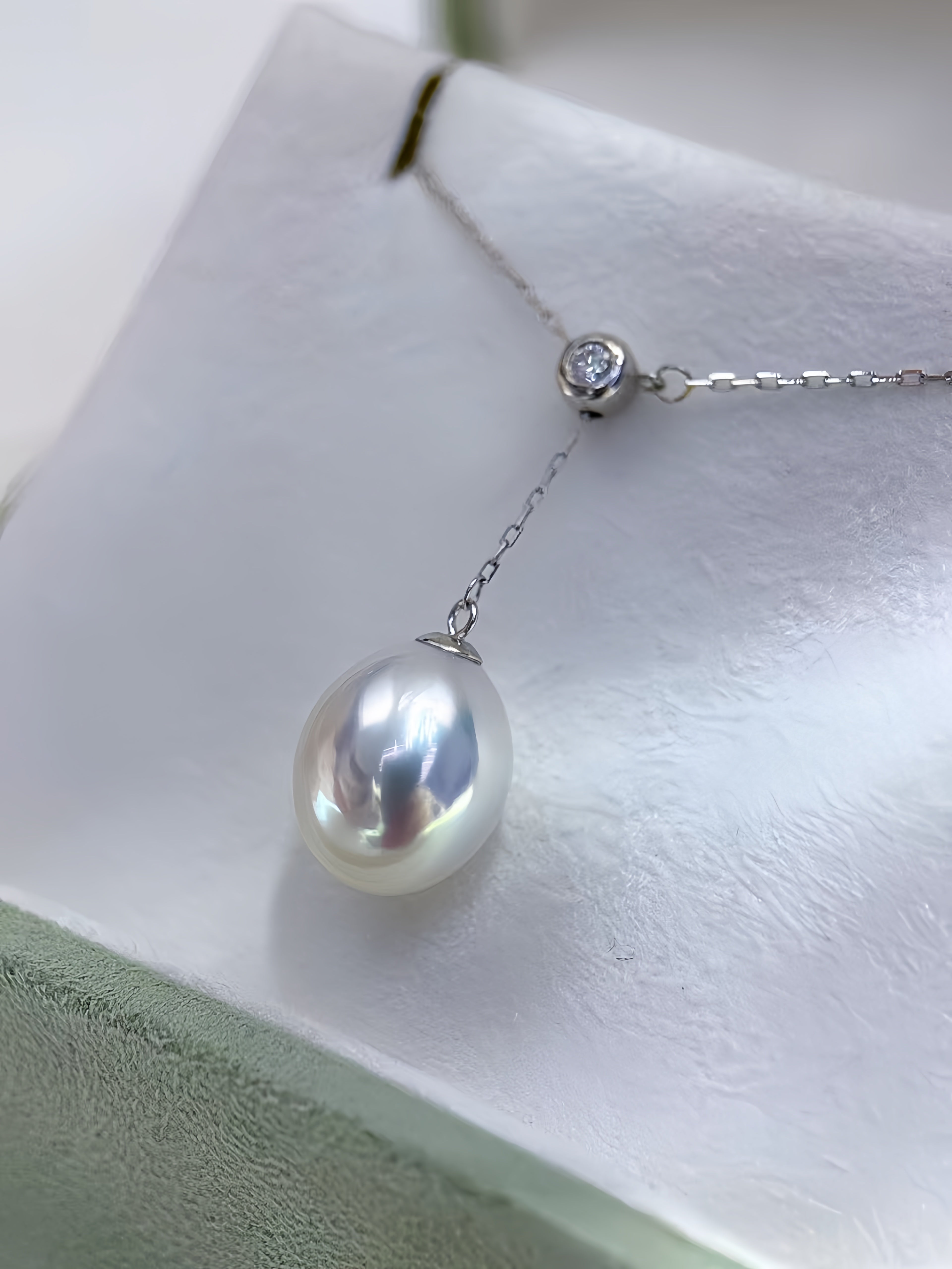A silver Y-shaped pendant necklace featuring a large, lustrous white baroque pearl and a small round clear gemstone, displayed on a white jewelry stand.
