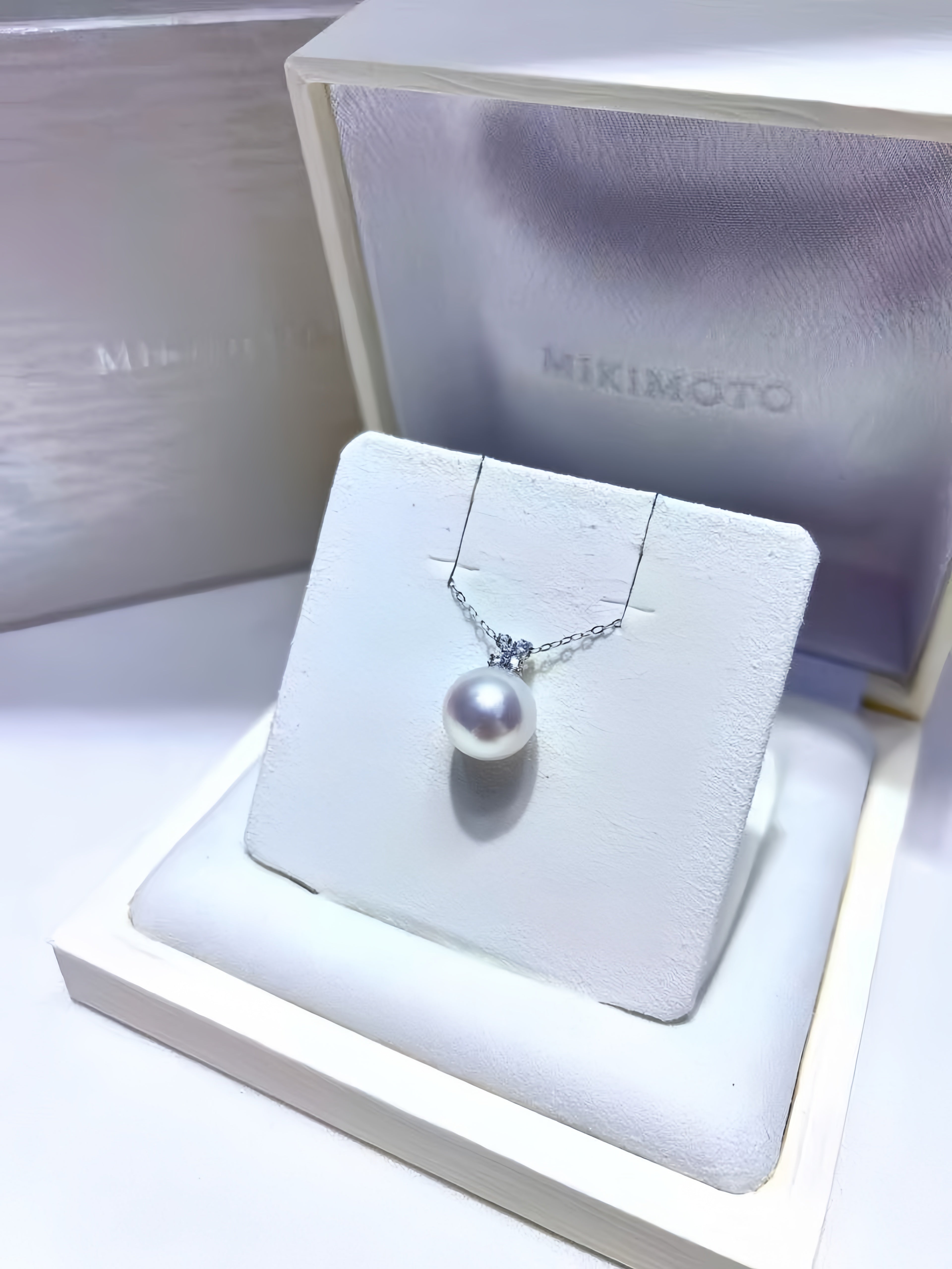 A Mikimoto brand silver necklace with a single white pearl pendant, displayed on a white jewelry stand inside an open cream-colored presentation box.