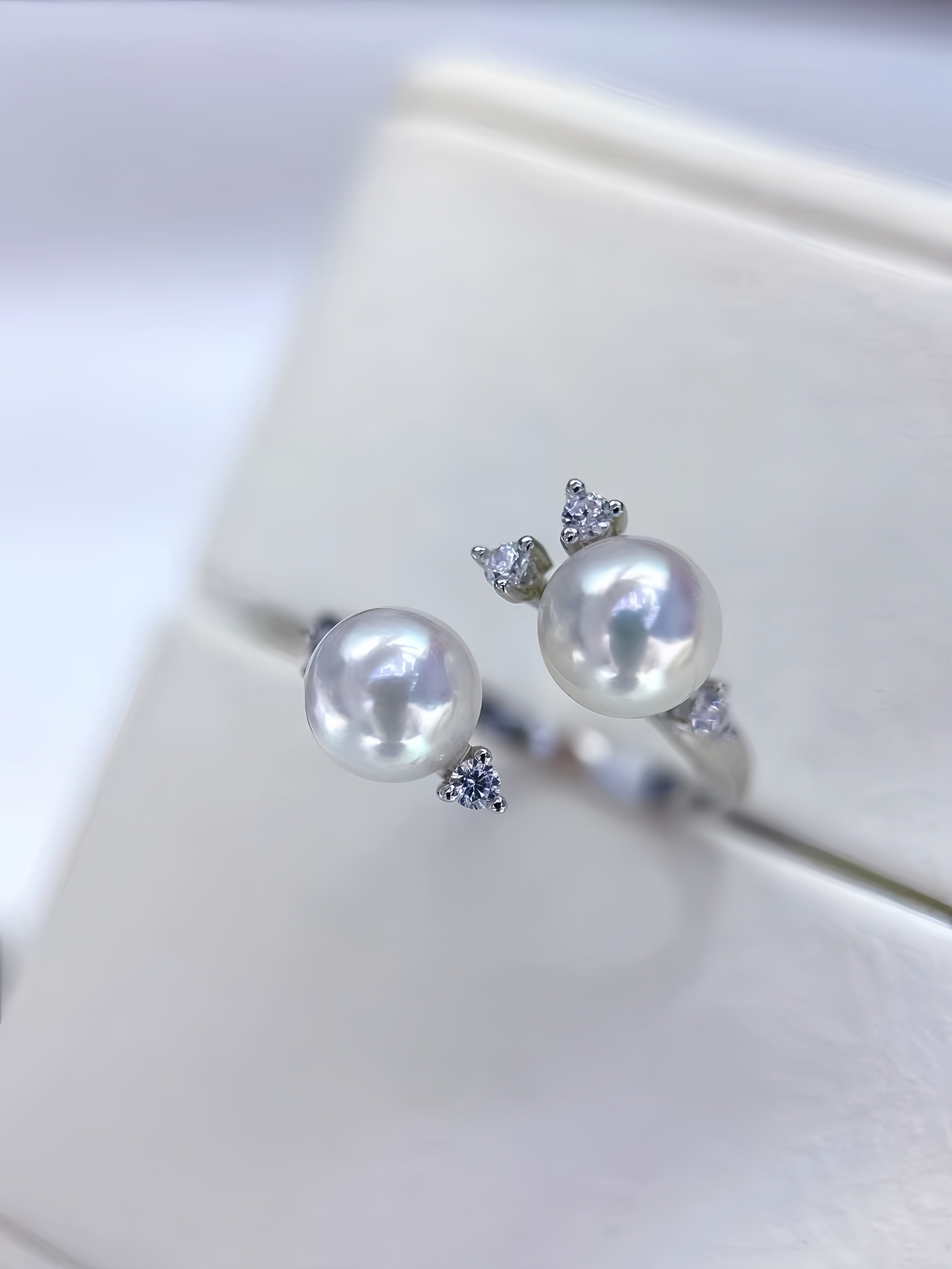 A pair of silver rings with large white pearls and small clear gemstone accents, displayed on a white jewelry box.