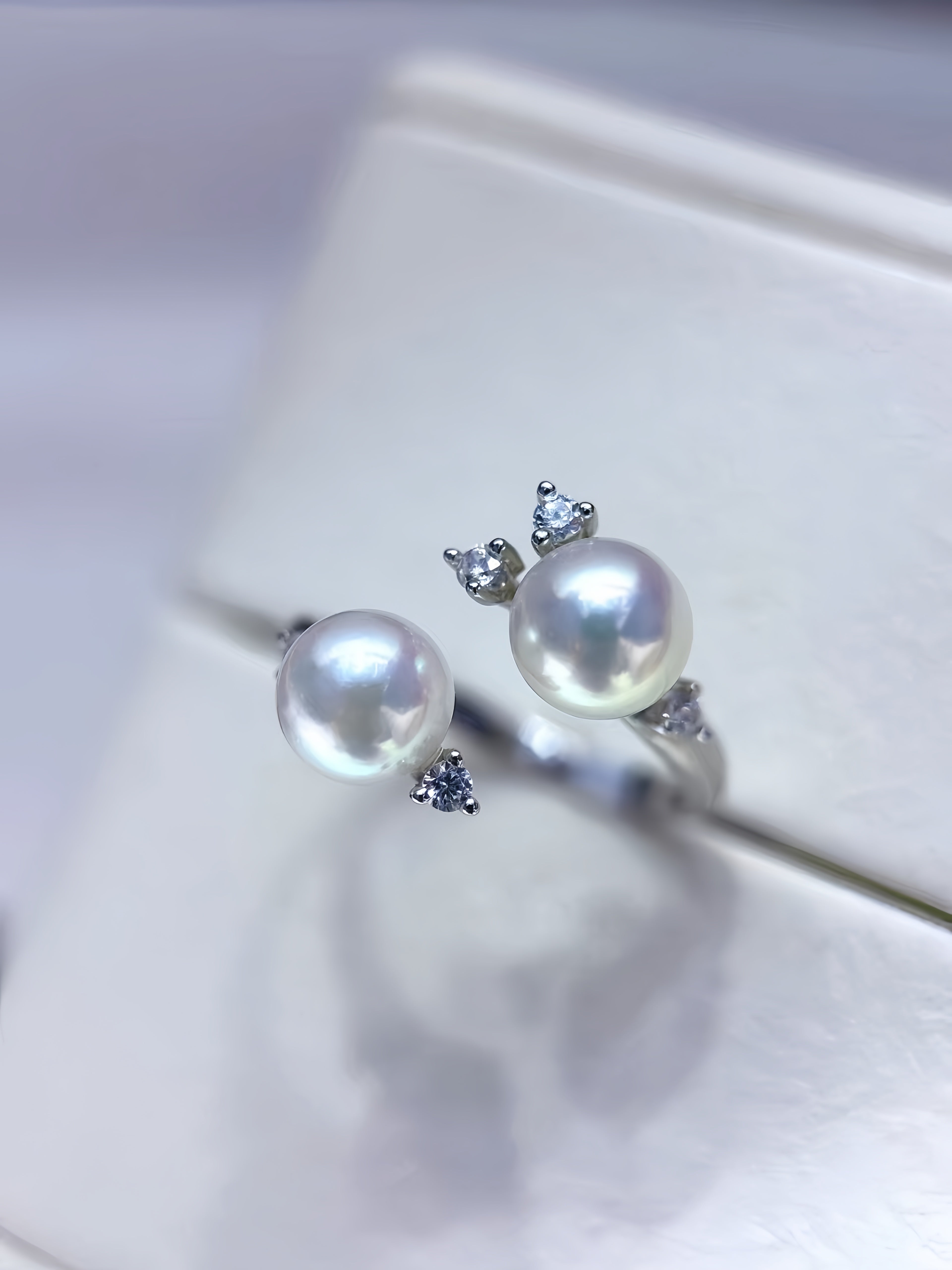 A pair of silver rings with large white freshwater pearls and small clear accent stones, displayed on a white jewelry box.