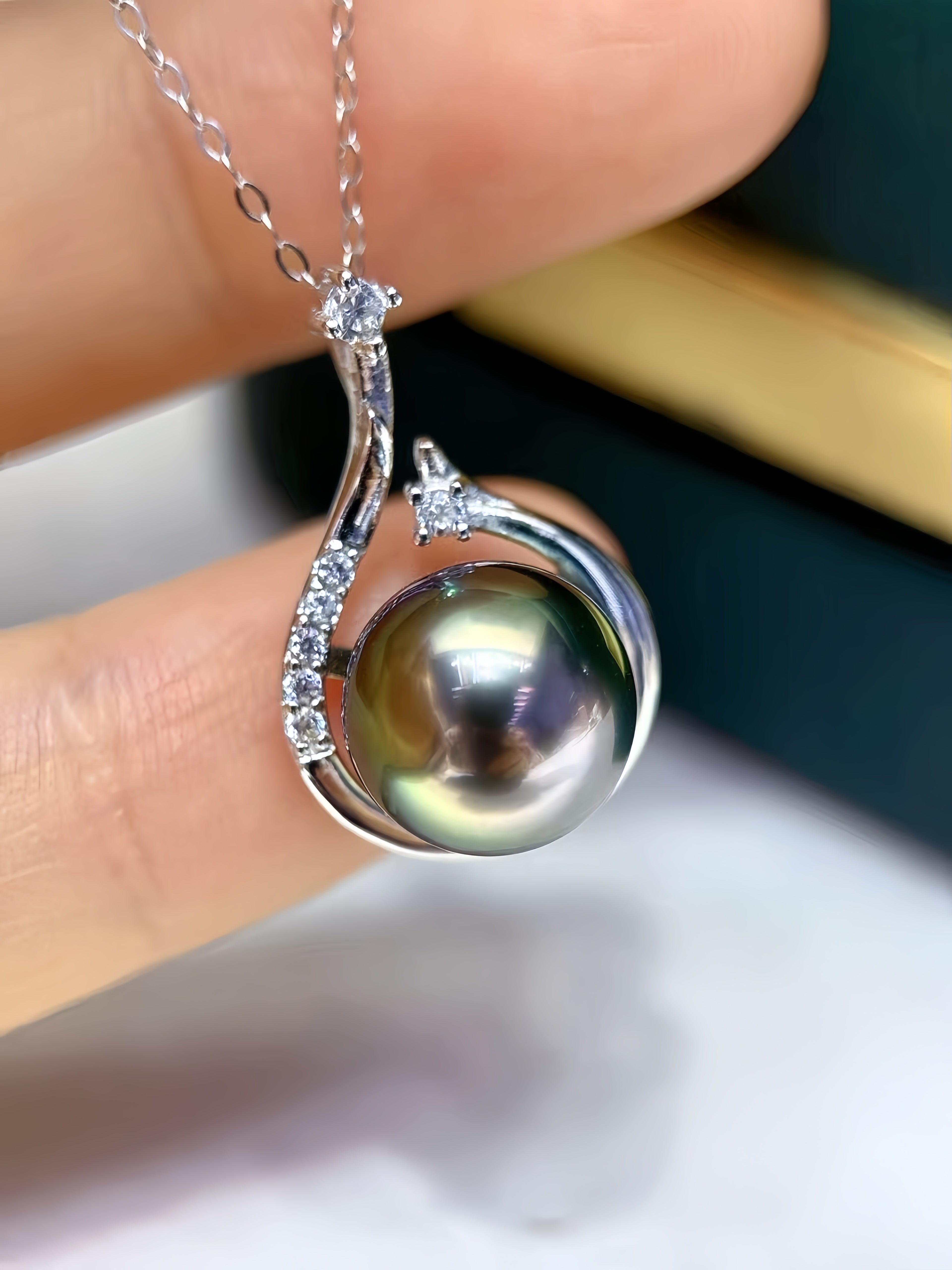 A close-up of a silver pendant necklace with a large iridescent freshwater pearl and small clear stones, held between fingers.