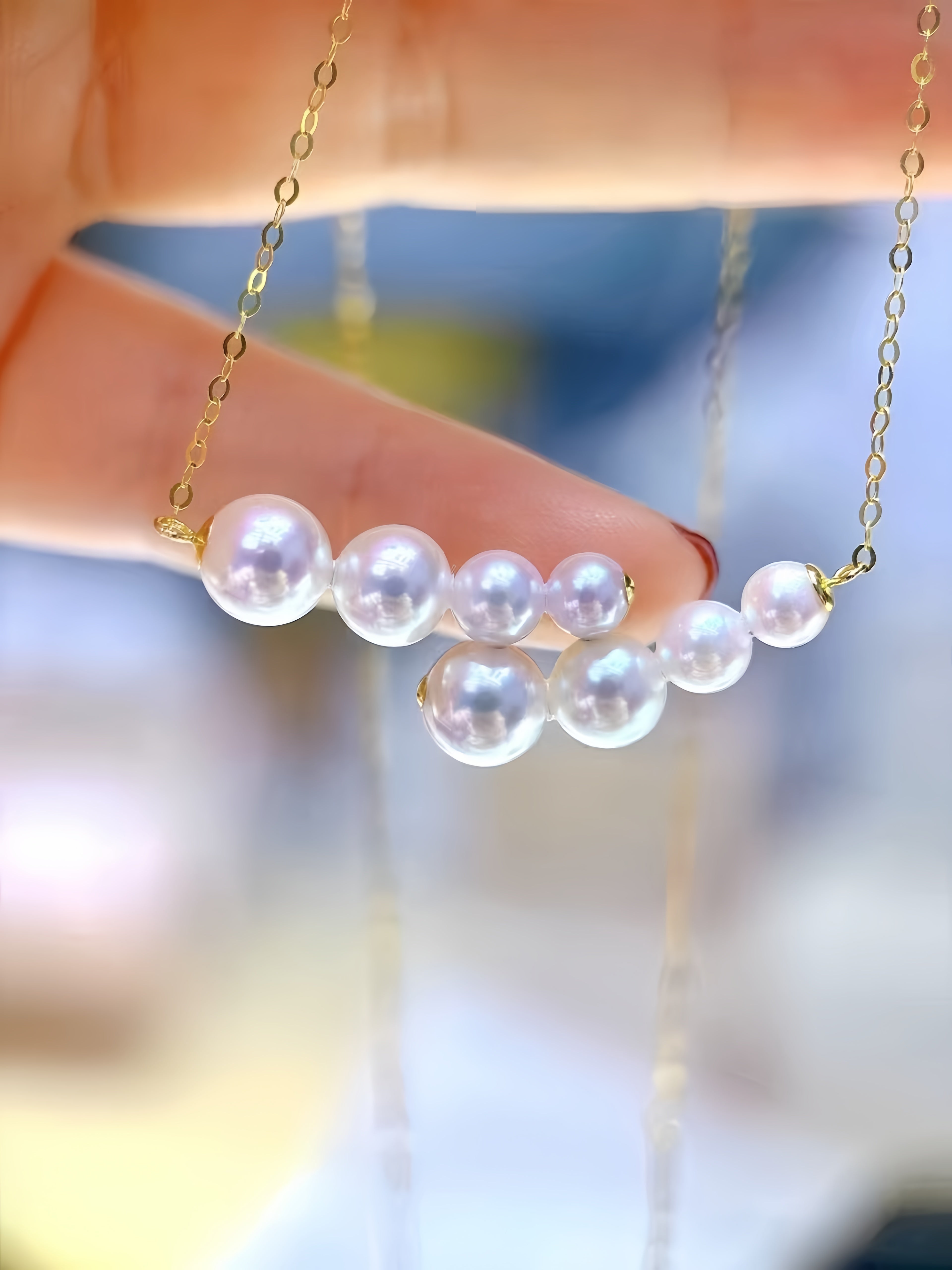 A close-up of a hand holding a delicate gold chain necklace with a row of white pearl-like beads as the centerpiece, against a softly blurred background.