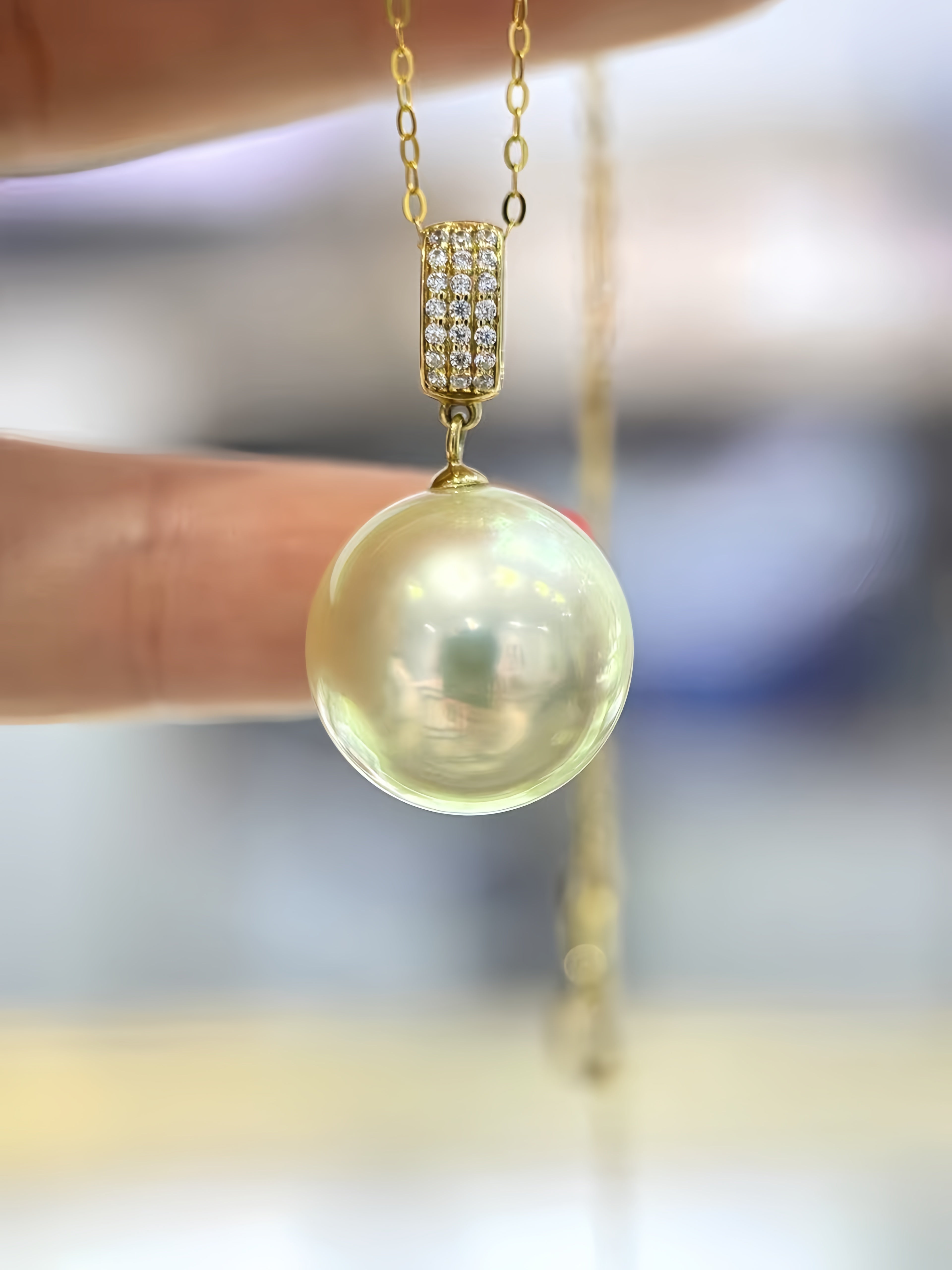 A close-up of a gold necklace with a large, lustrous pearl pendant held by fingers against a softly blurred background.