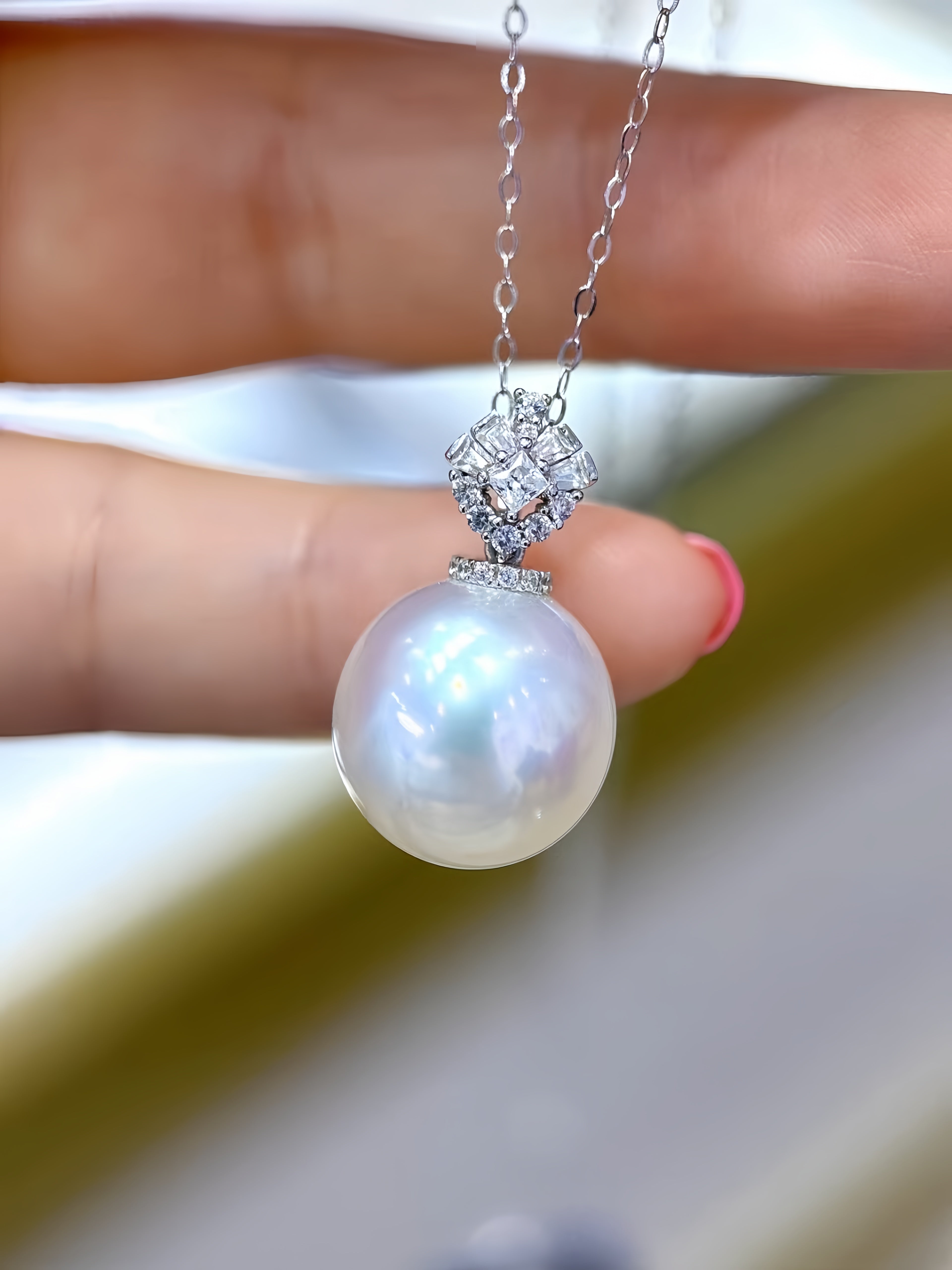 A close-up of a hand holding a silver chain necklace with a large, lustrous white pearl pendant and a sparkling silver pavé setting.