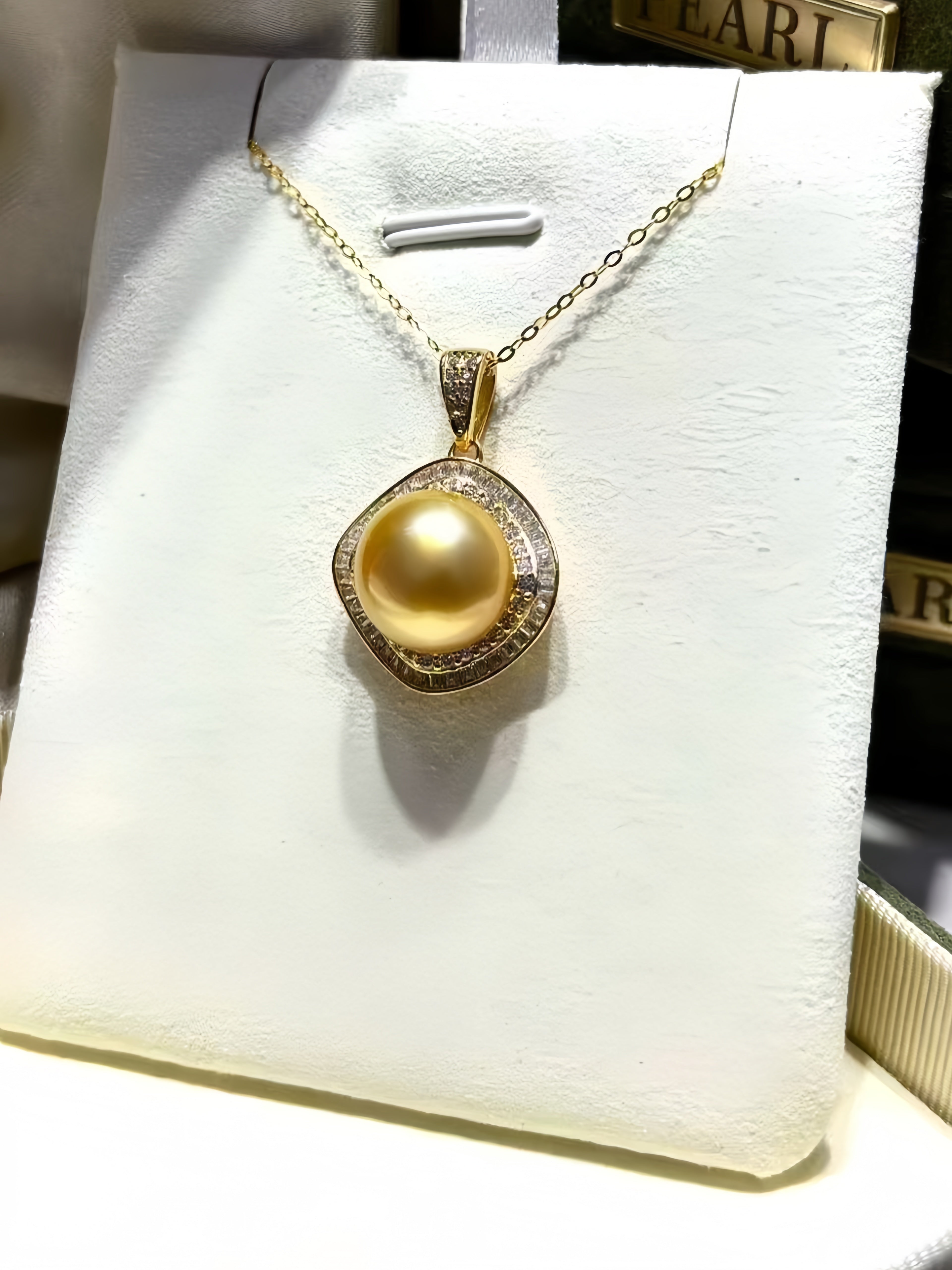 A gold pendant necklace featuring a large round yellow pearl surrounded by a halo of small clear stones, displayed on a white jewelry stand.