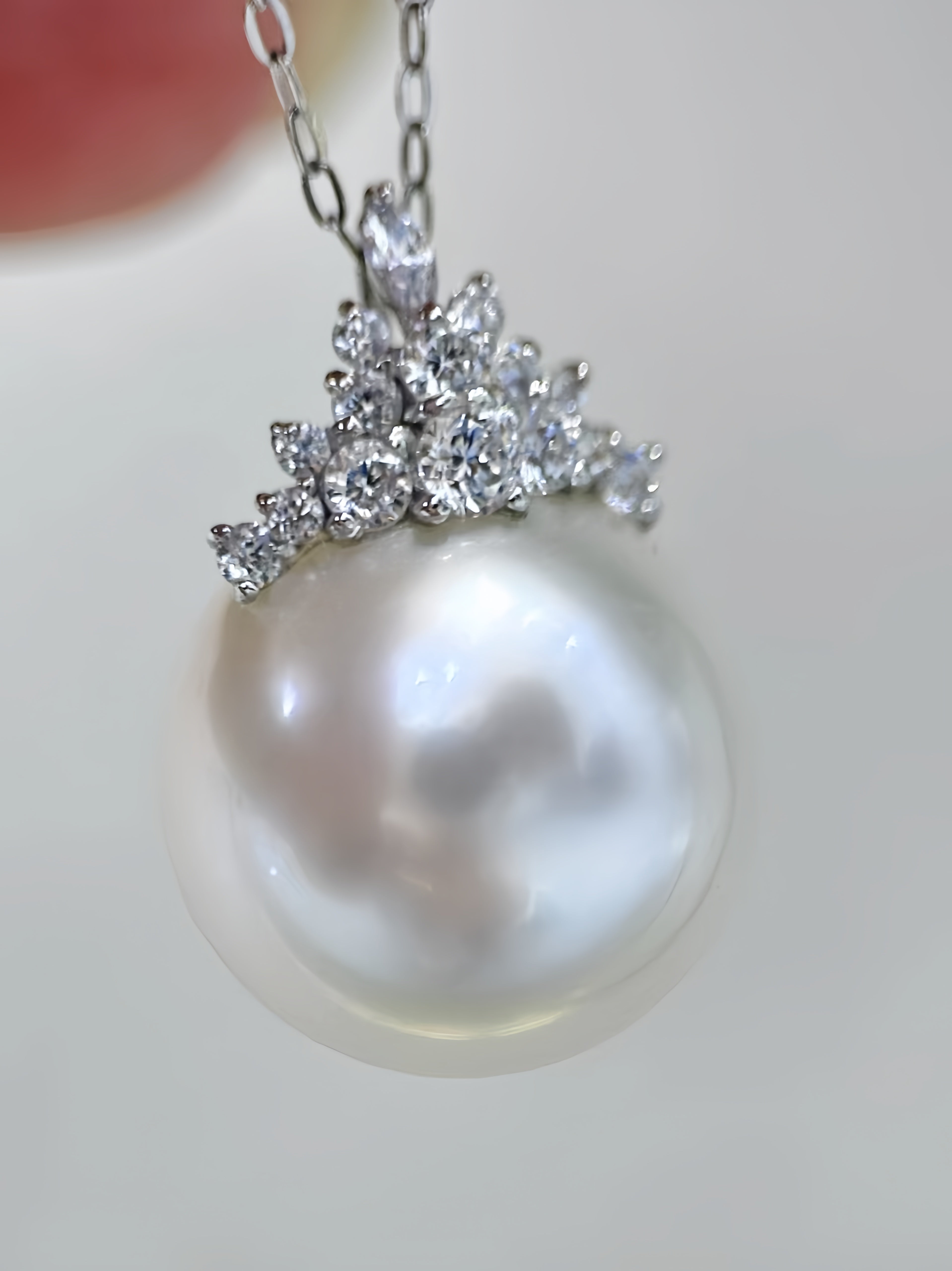 A close-up of a pearl pendant necklace with a silver-toned floral halo set with clear stones, hanging from a delicate chain.