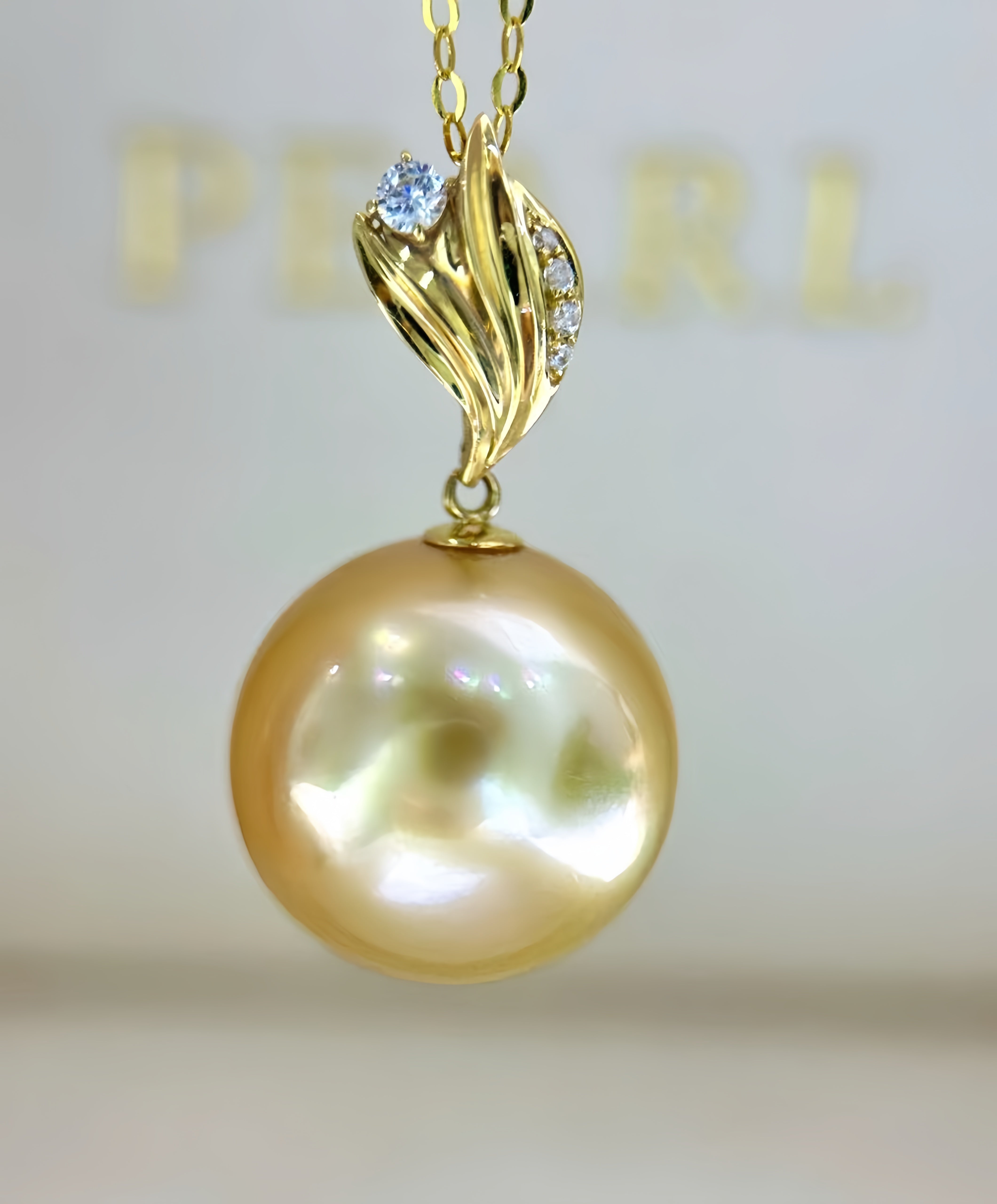 A gold pendant necklace featuring a large, lustrous golden pearl suspended from a gold chain with a decorative gold bail accented by small clear stones.
