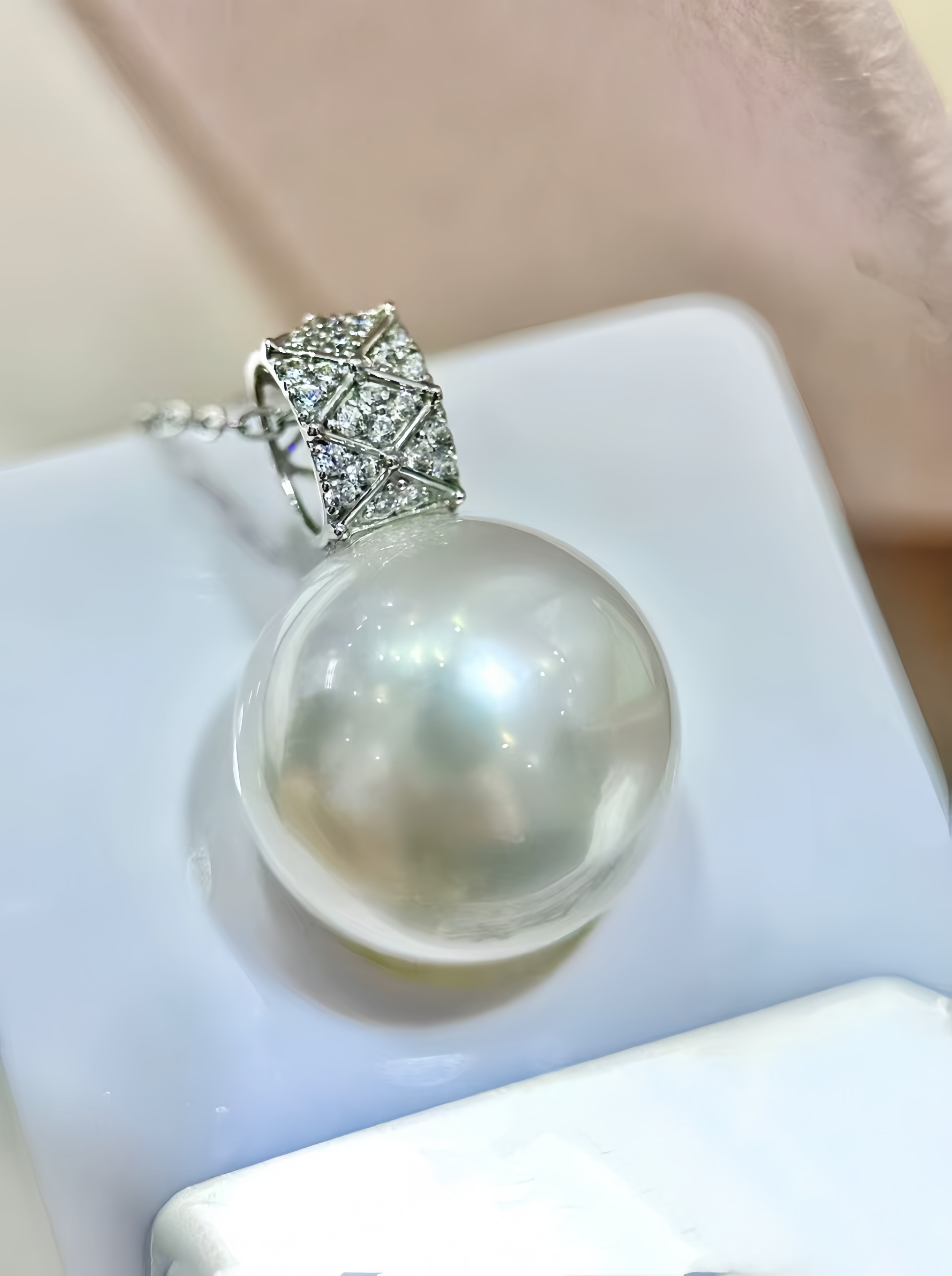 A close-up of a pearl pendant necklace with a silver-toned woven bail, resting on a white display stand.