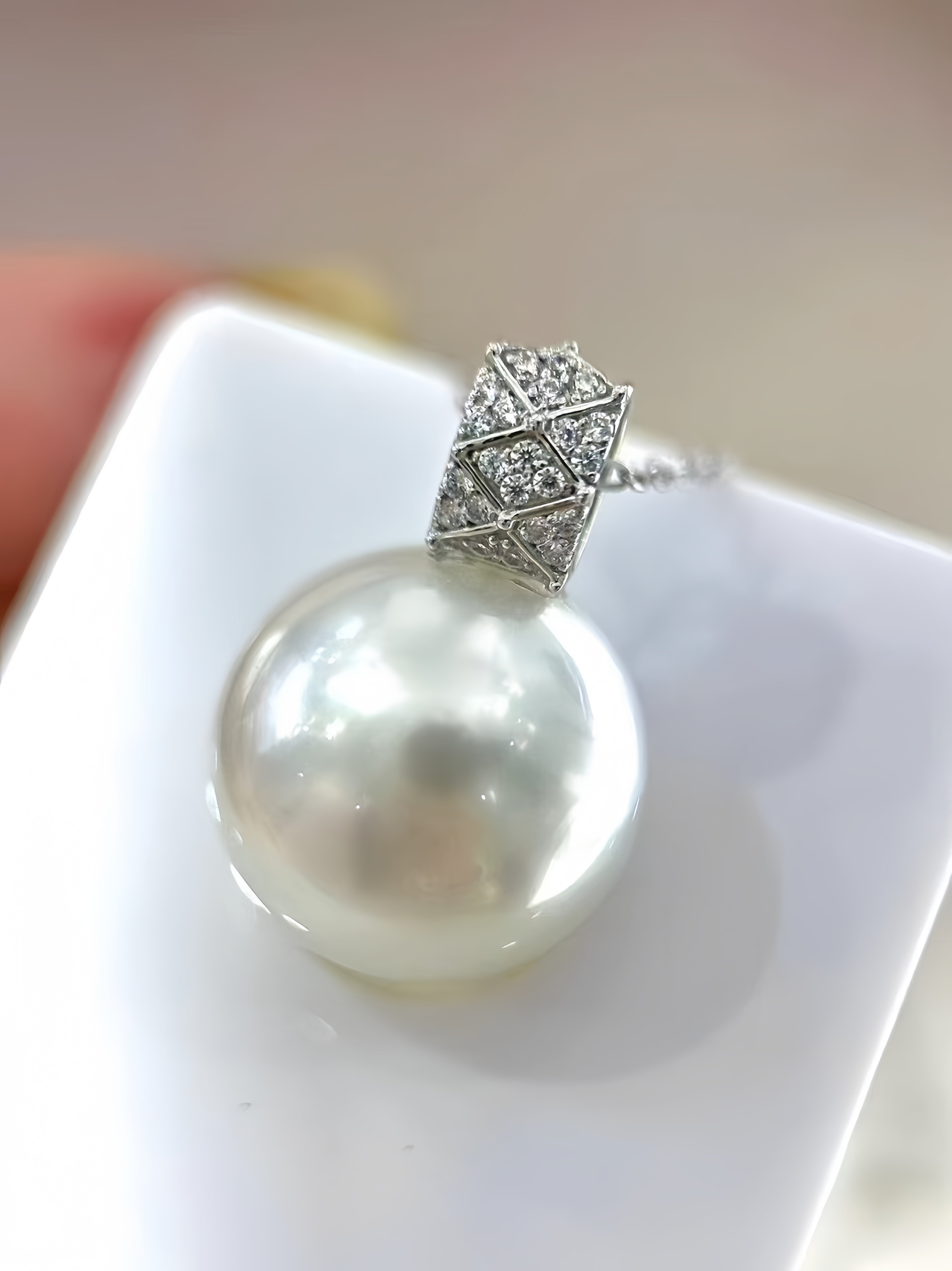 A close-up of a white freshwater pearl pendant with a silver pavé geometric cap, resting on a white display block.