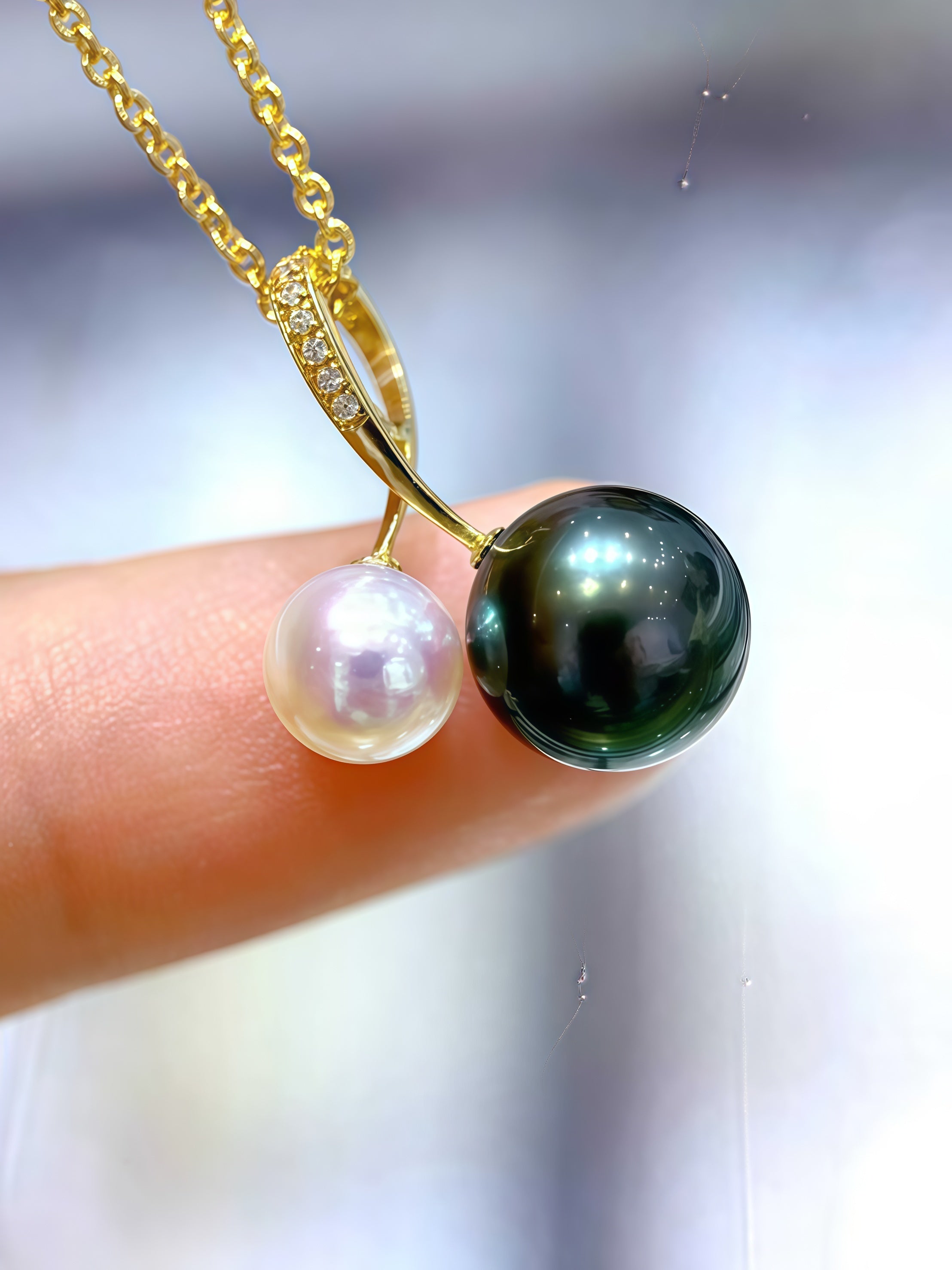 Gold necklace with a black and white pearl pendant held between fingers against a blurred background