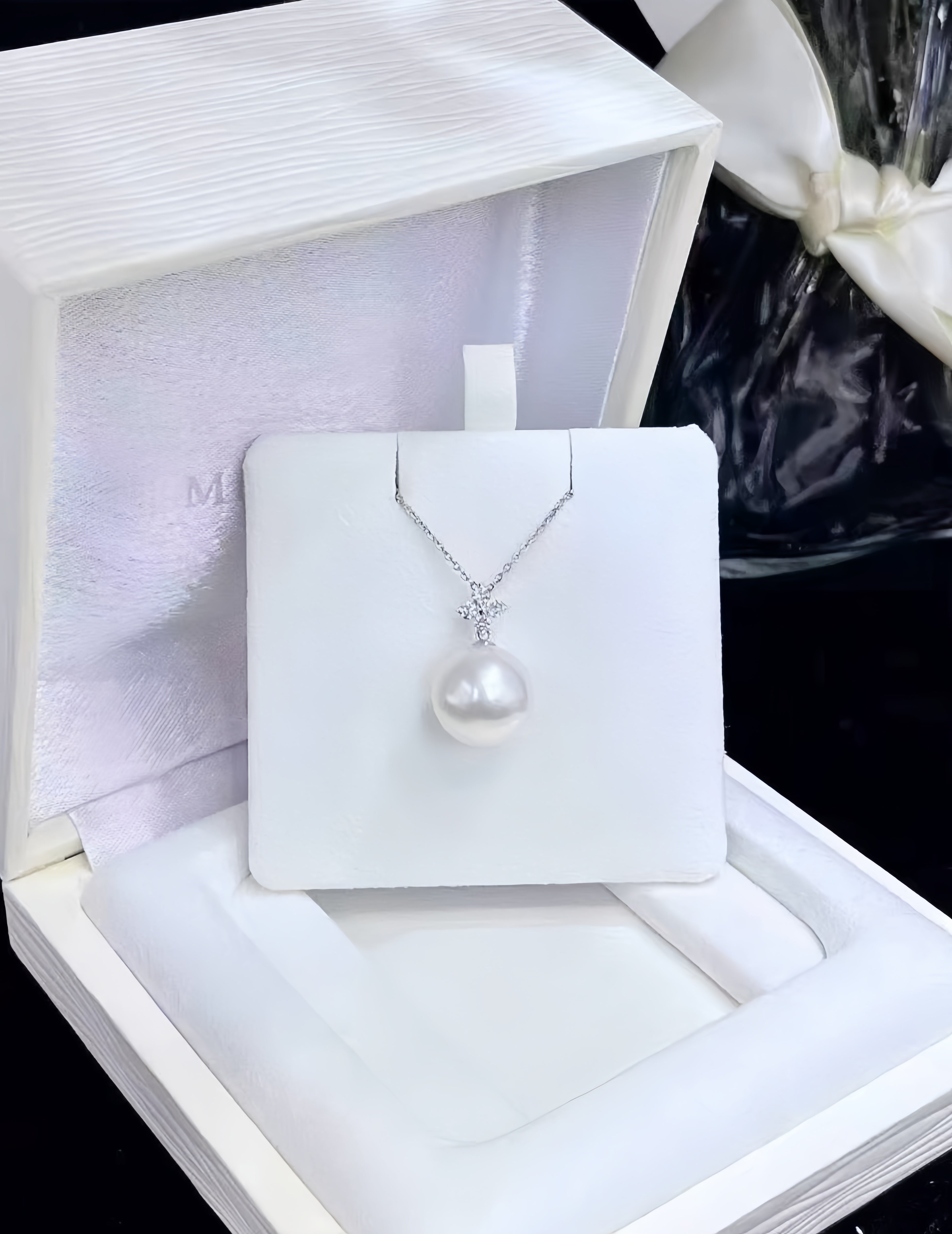 A silver necklace with a large white freshwater pearl pendant displayed on a white jewelry card, set inside an open white presentation box.