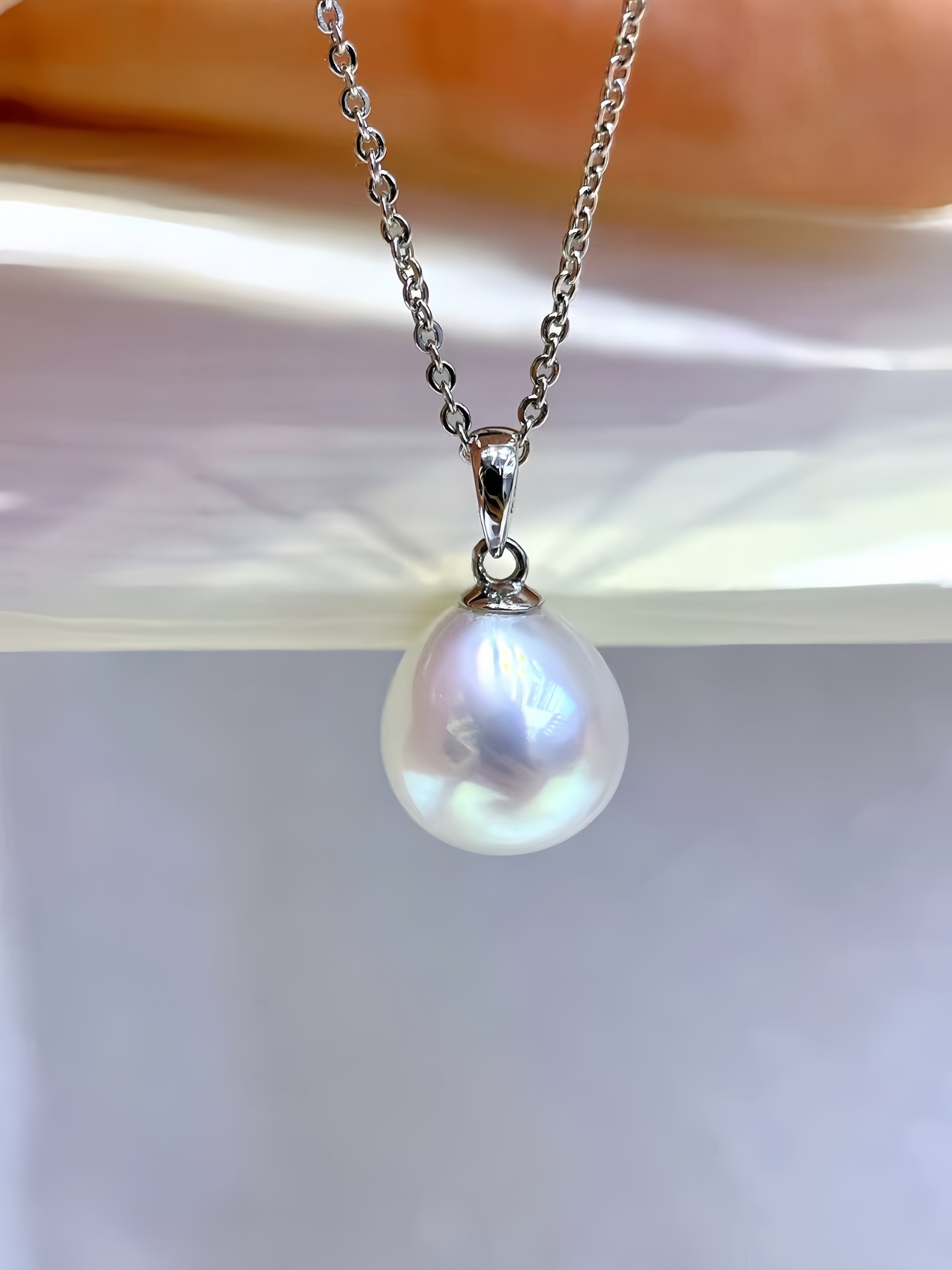 A silver chain necklace with a single teardrop-shaped white pearl pendant, held against a soft white background.