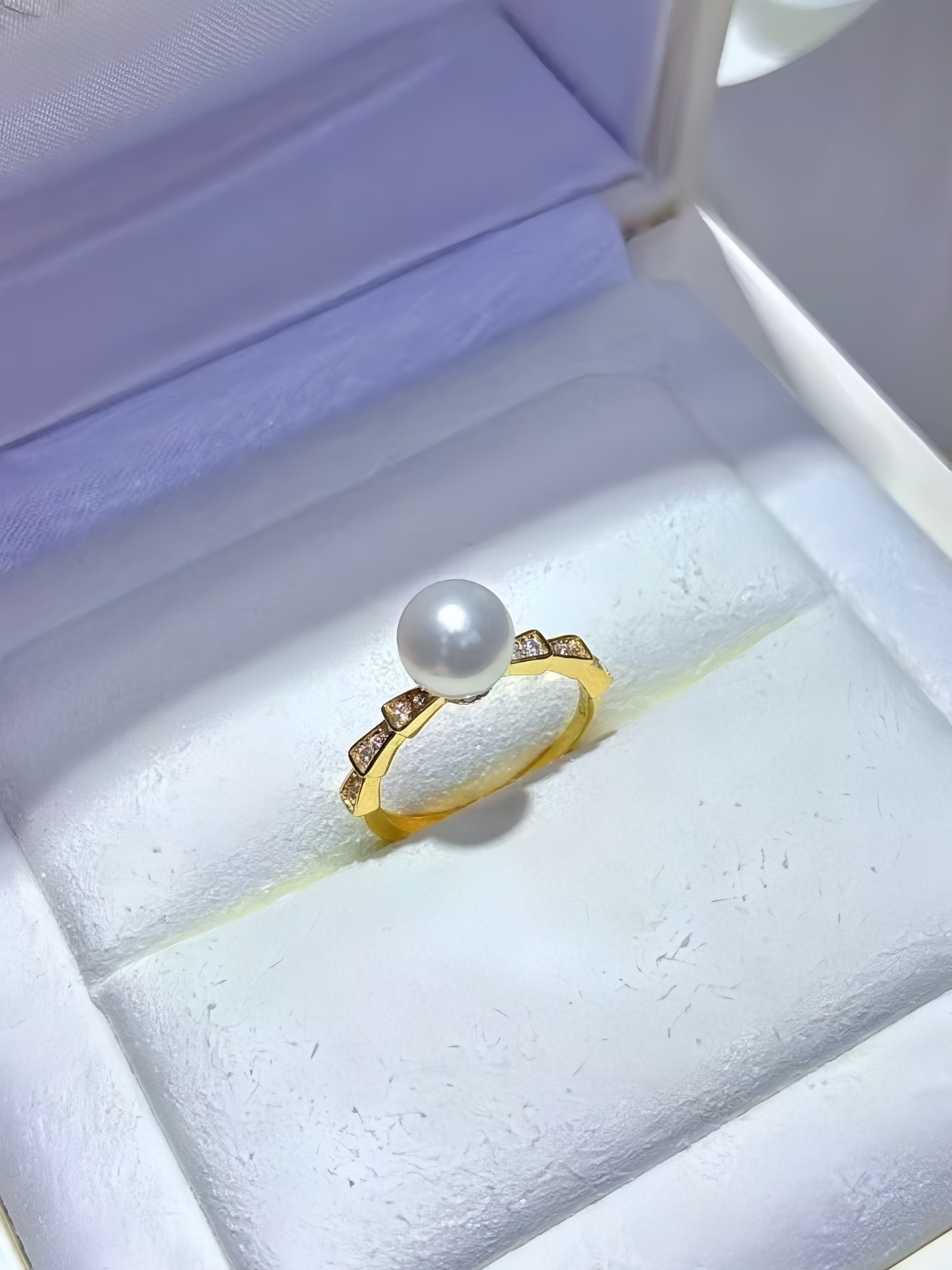 A gold ring with a single white pearl and small clear stones, displayed in a white jewelry box.