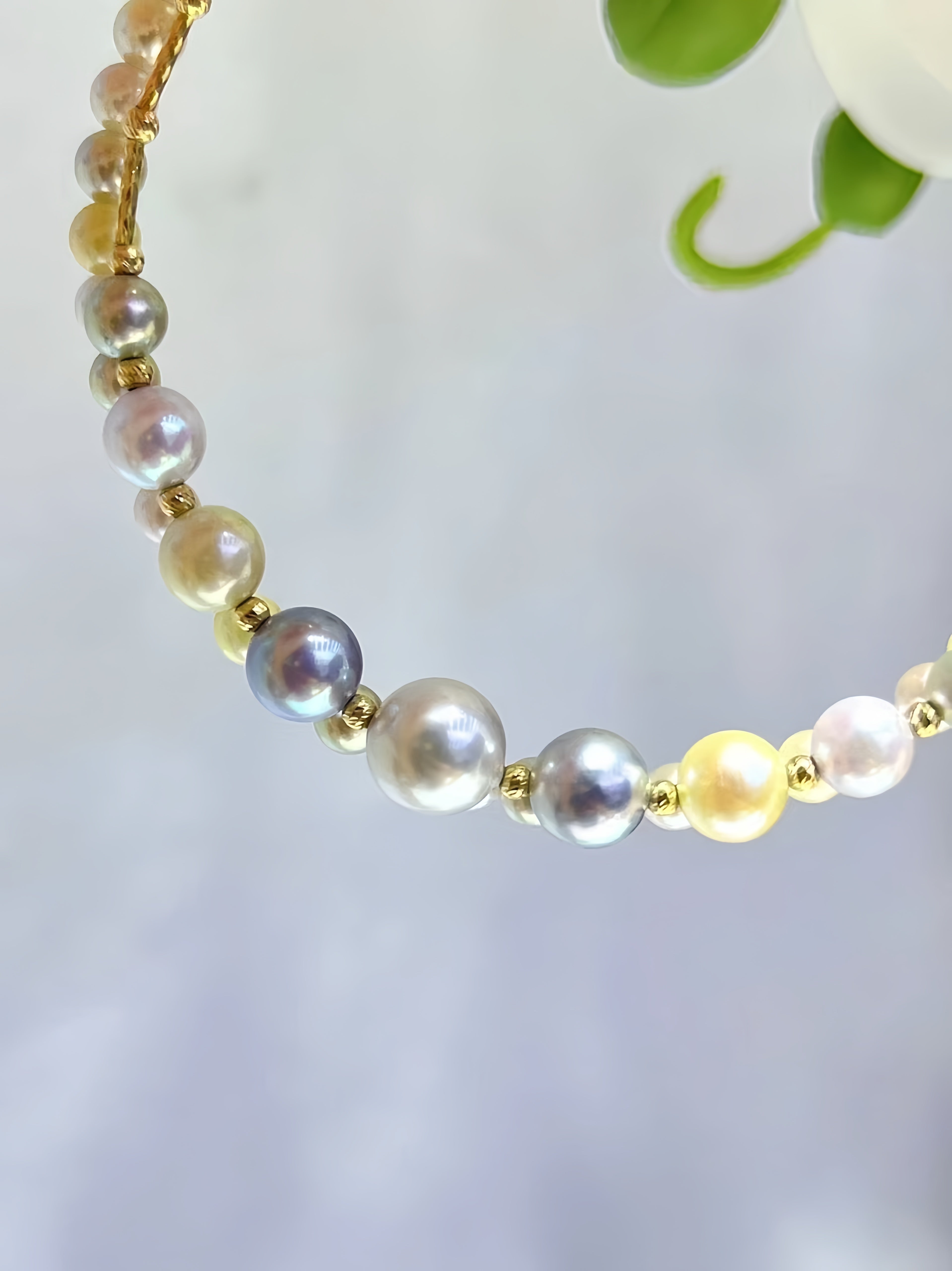 A close-up of a beaded necklace featuring a mix of iridescent freshwater pearls in white, cream, yellow, and gray, separated by small gold spacer beads.