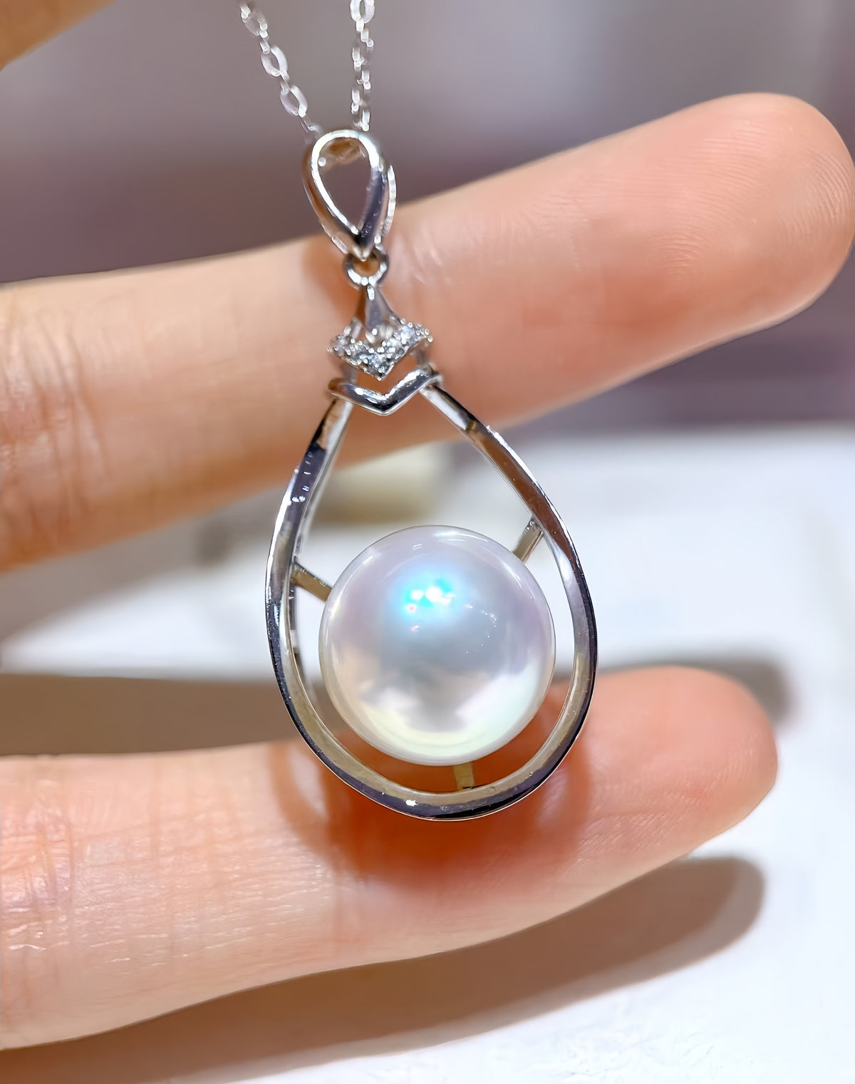 A teardrop-shaped pearl pendant in a silver-toned setting, displayed on a white jewelry card inside an open cream-colored presentation box.