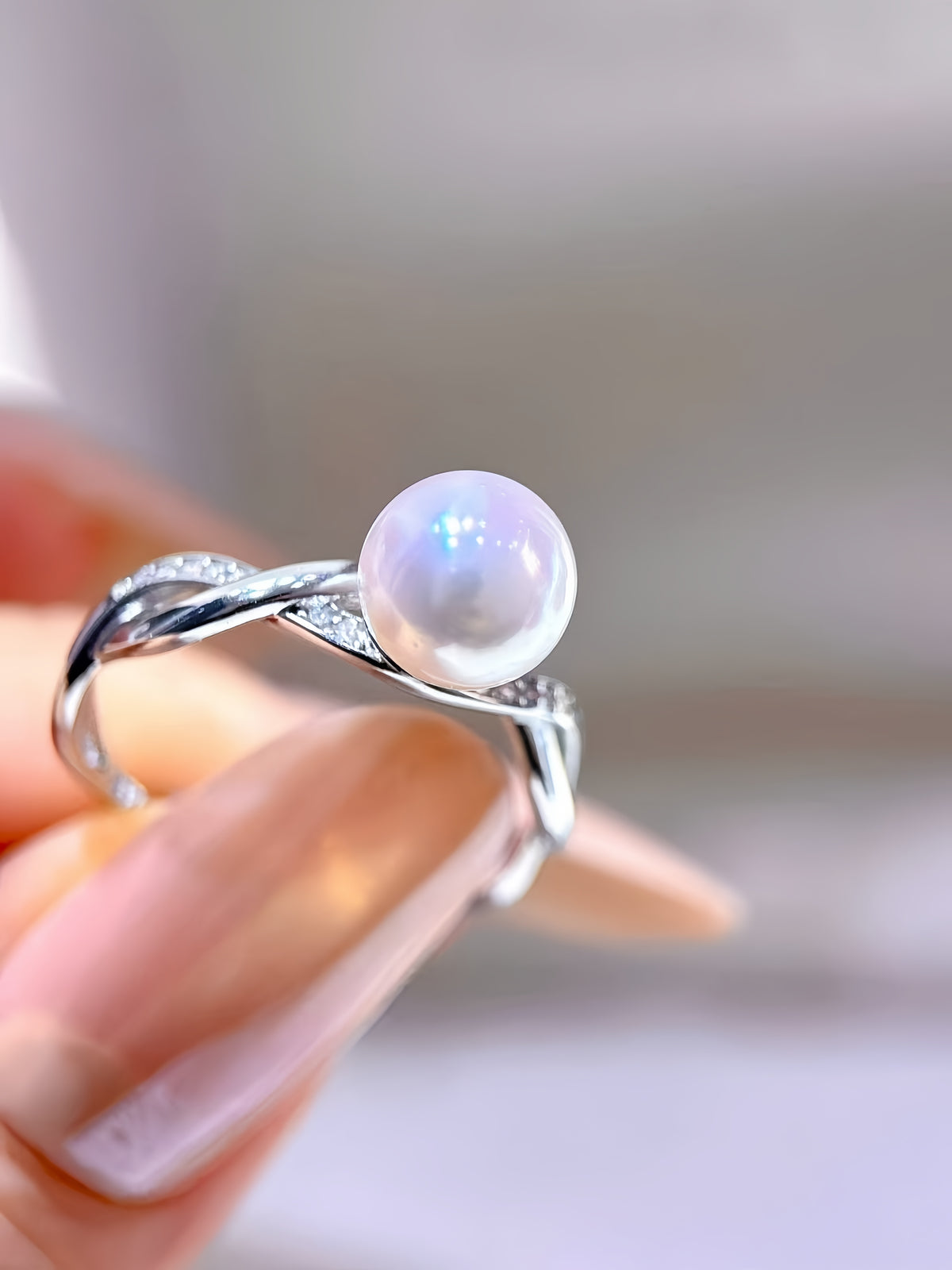 A silver ring with a round white pearl and small clear stones, displayed in an open dark blue heart-shaped jewelry box held in a hand.