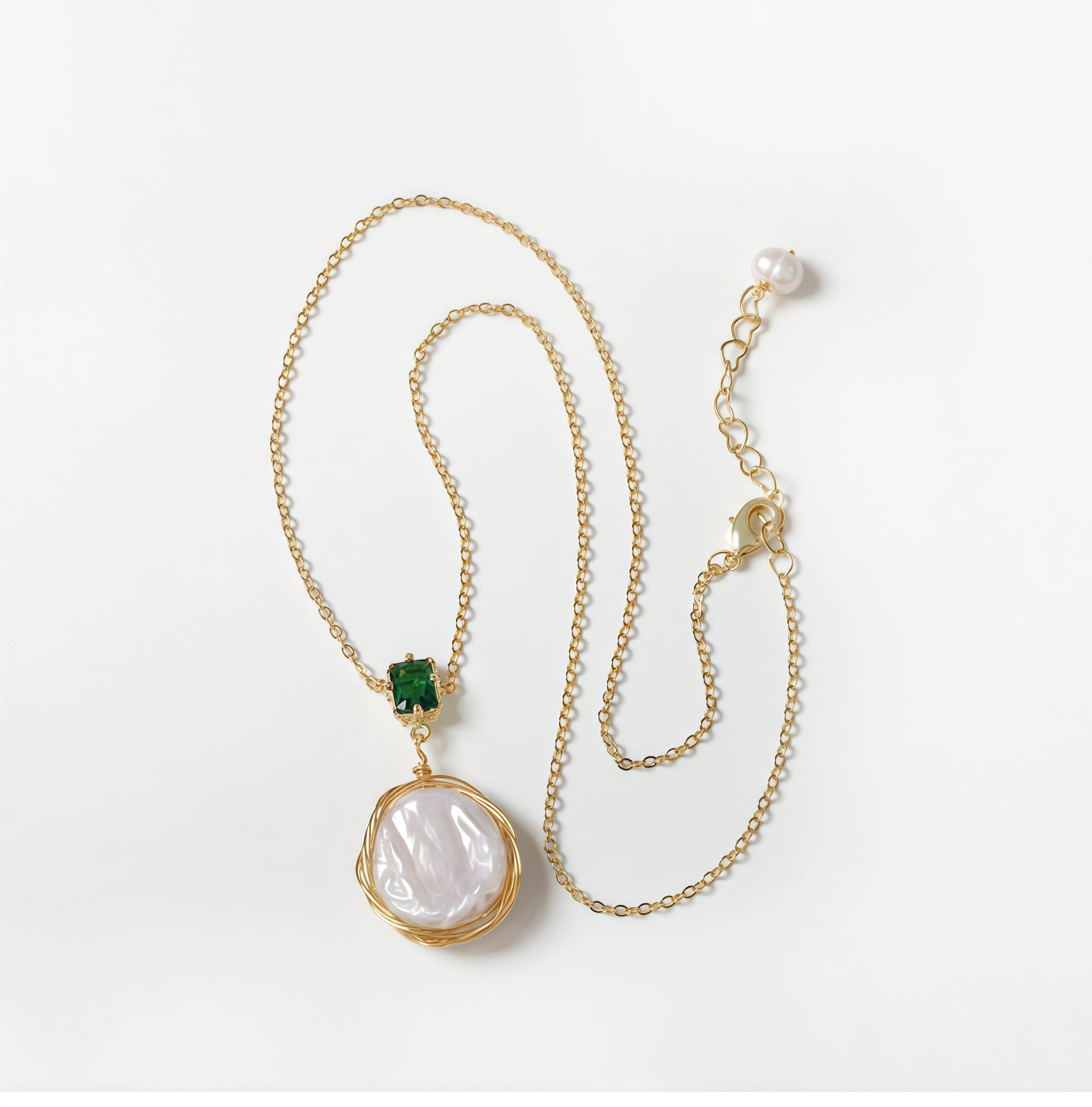 Close-up of white irregular baroque freshwater pearl, coin-shaped pendant, wire wrapped with green cubic zirconia